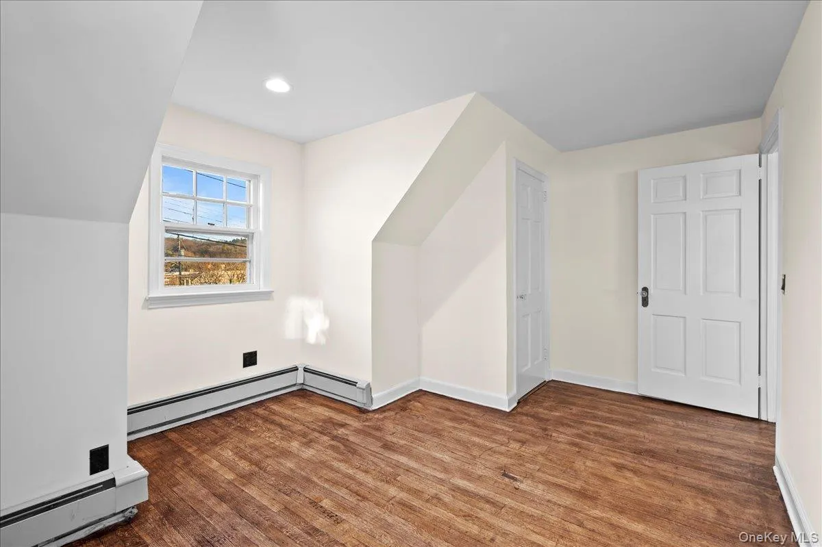 Room featuring wood-finish flooring, a double-hung window, and two paneled doors with dark hardware Room featuring wood-finish flooring, a double-hung window, and two paneled doors with dark hardware