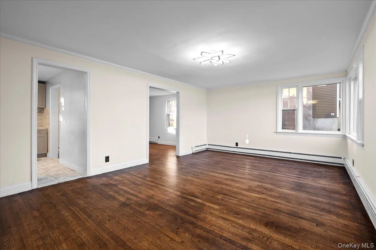 Spacious room featuring rich wood-finish flooring, light-toned walls, and multiple windows with white trim Spacious room featuring rich wood-finish flooring, light-toned walls, and multiple windows with white trim
