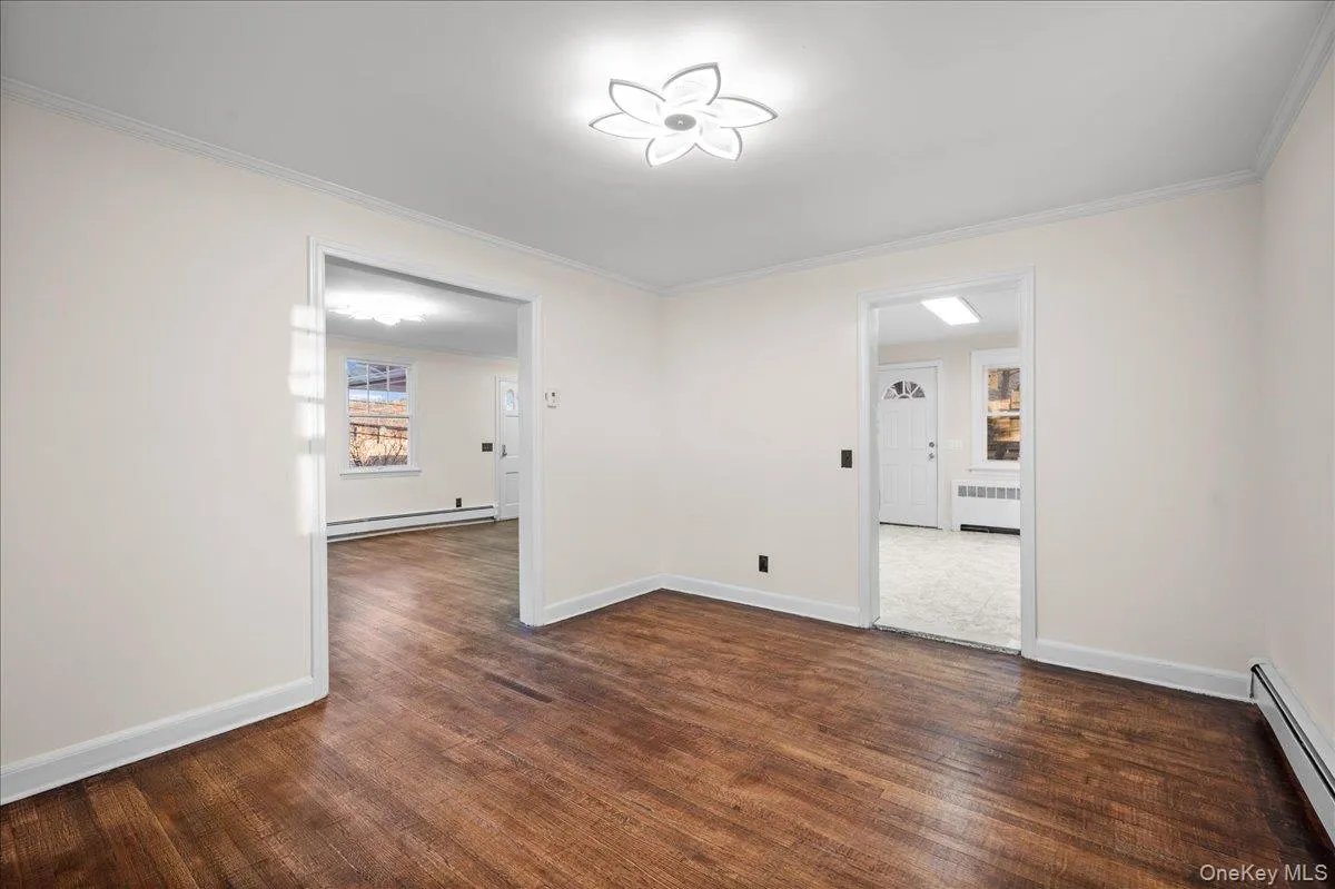 Interior room featuring wood-finish flooring, white baseboards, and crown molding Interior room featuring wood-finish flooring, white baseboards, and crown molding