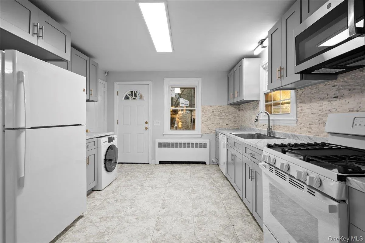 Kitchen featuring gray cabinetry, stone-finish backsplash, built-in microwave, gas range, and a full-size refrigerator Kitchen featuring gray cabinetry, stone-finish backsplash, built-in microwave, gas range, and a full-size refrigerator