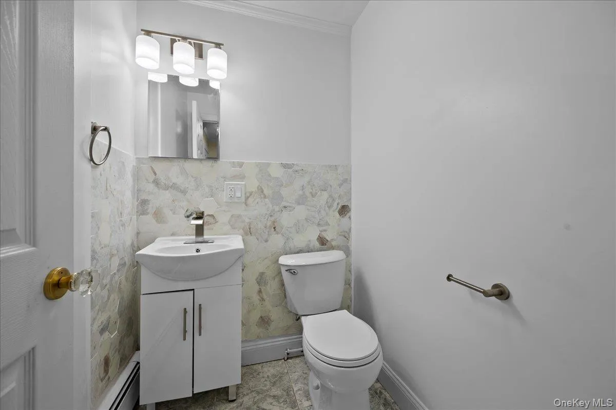 Bathroom featuring a modern vanity with integrated sink, contemporary wall sconce lighting, mosaic-style tile wainscoting, and a clear crystal doorknob Bathroom featuring a modern vanity with integrated sink, contemporary wall sconce lighting, mosaic-style tile wainscoting, and a clear crystal doorknob