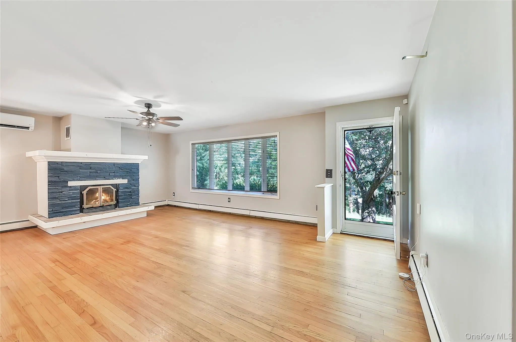 Unfurnished living room featuring a fireplace, a baseboard heating unit, light wood-style flooring, baseboard heating, and an AC wall unit Unfurnished living room featuring a fireplace, a baseboard heating unit, light wood-style flooring, baseboard heating, and an AC wall unit