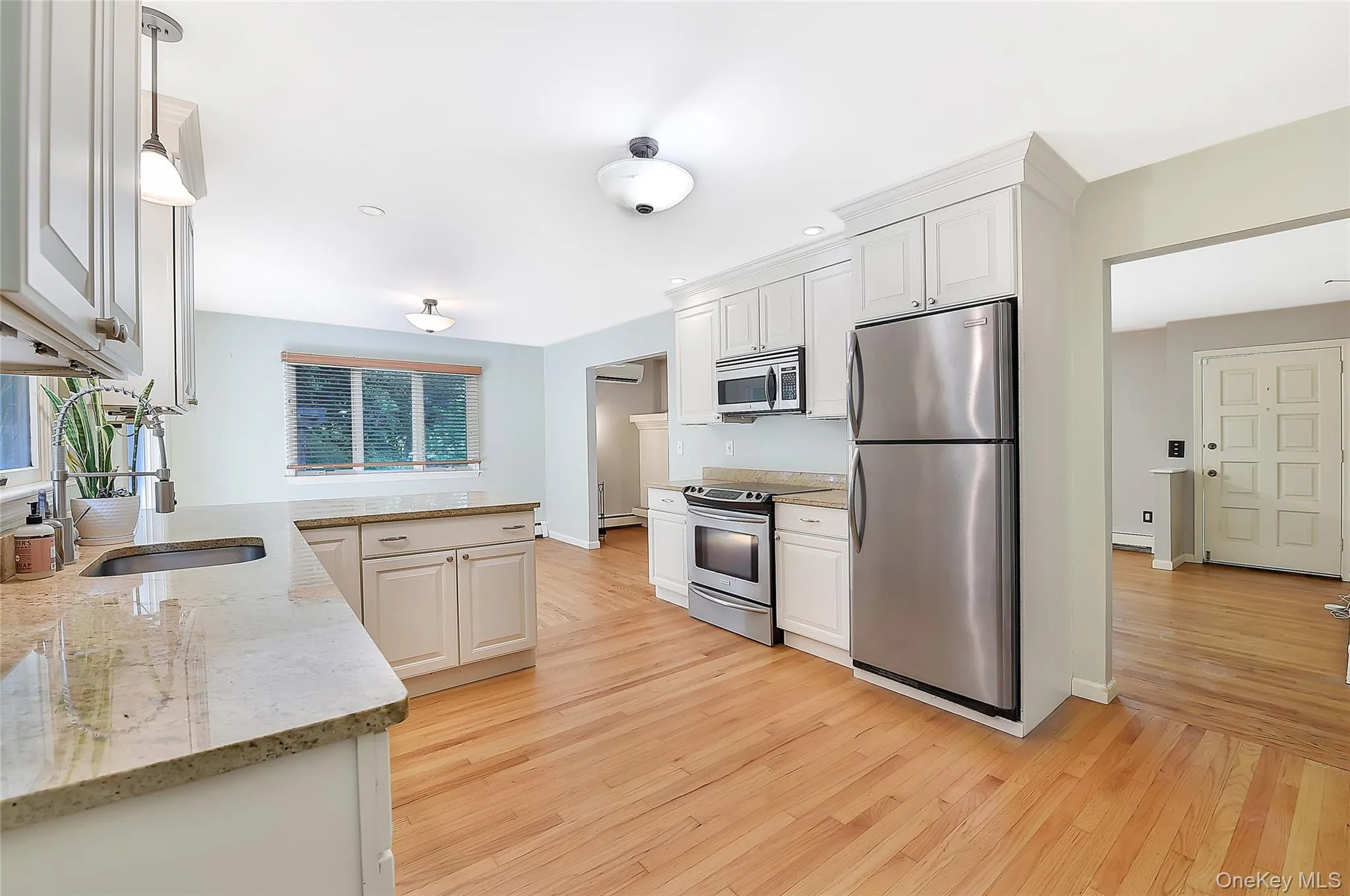 Kitchen with appliances with stainless steel finishes, light stone counters, light wood finished floors, white cabinets, and pendant lighting Kitchen with appliances with stainless steel finishes, light stone counters, light wood finished floors, white cabinets, and pendant lighting