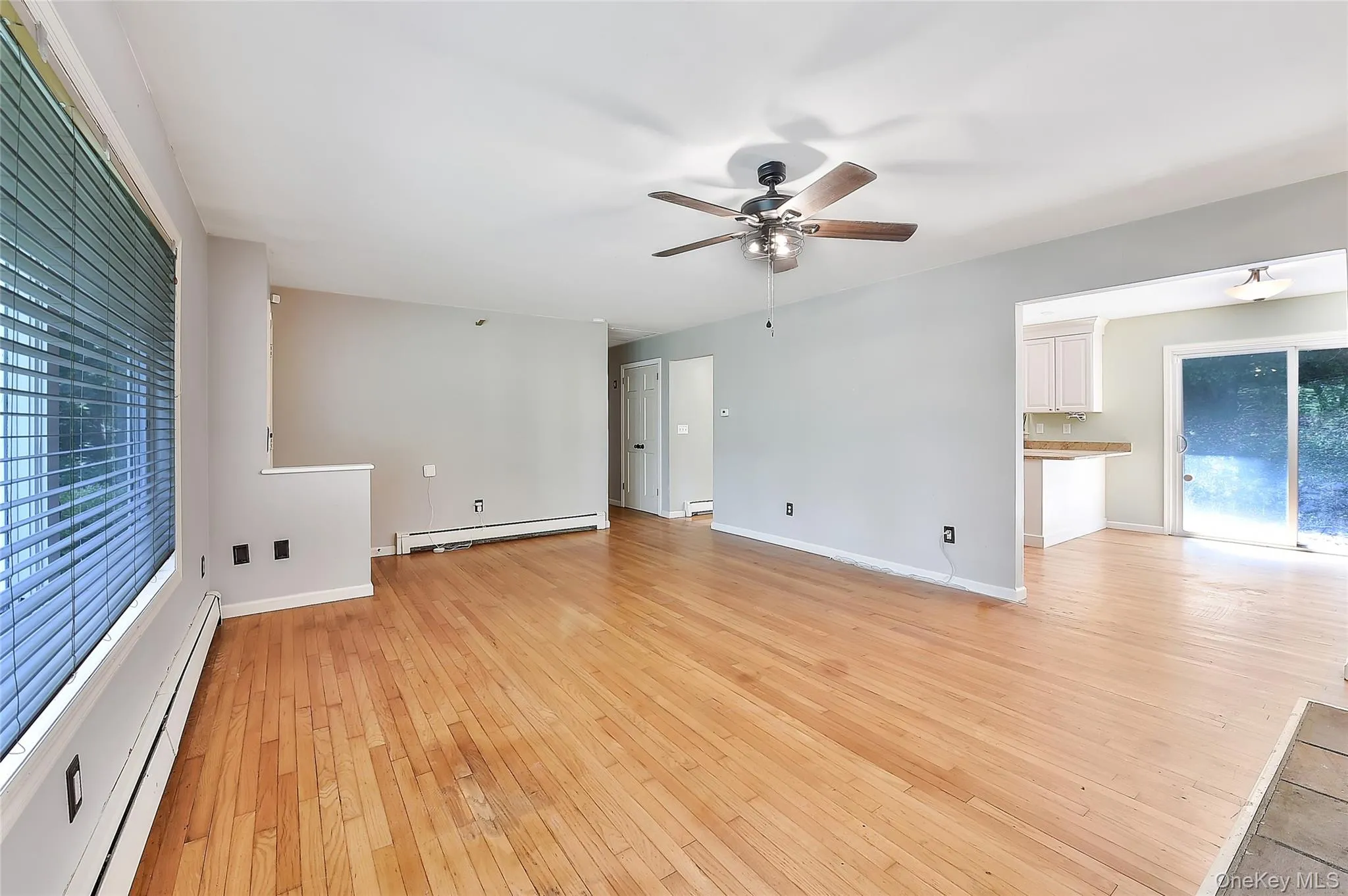 Unfurnished living room featuring a baseboard radiator, light wood-type flooring, ceiling fan, and baseboard heating Unfurnished living room featuring a baseboard radiator, light wood-type flooring, ceiling fan, and baseboard heating