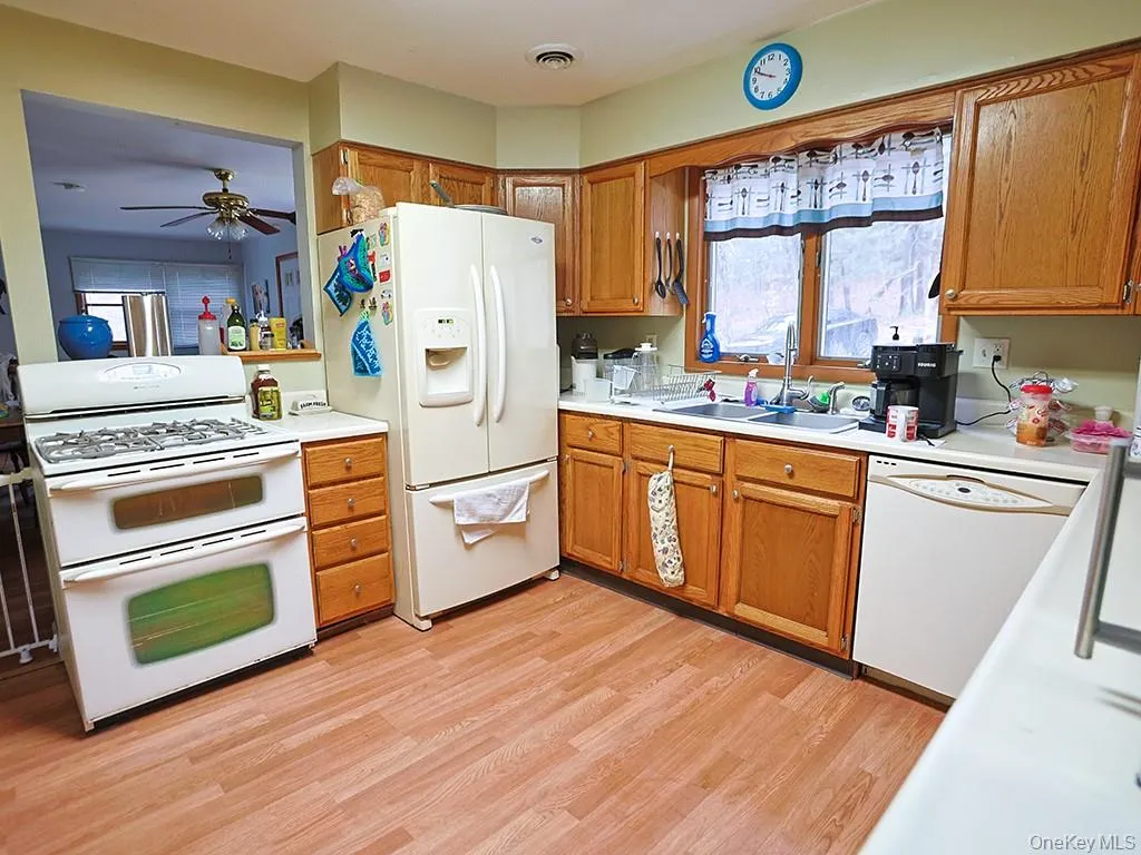 Kitchen with white appliances, light countertops, visible vents, brown cabinets, and a sink Kitchen with white appliances, light countertops, visible vents, brown cabinets, and a sink