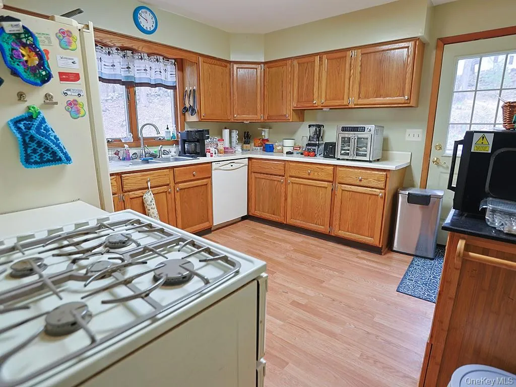 Kitchen featuring white appliances, brown cabinetry, light countertops, a sink, and light wood finished floors Kitchen featuring white appliances, brown cabinetry, light countertops, a sink, and light wood finished floors