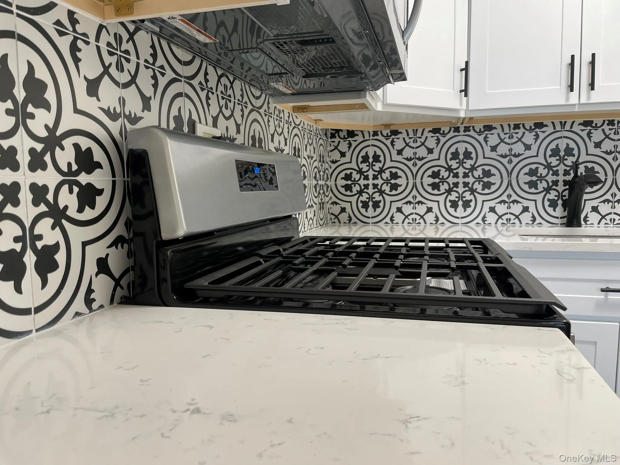 Kitchen with white cabinets, gas stove, light stone counters, and decorative backsplash Kitchen with white cabinets, gas stove, light stone counters, and decorative backsplash