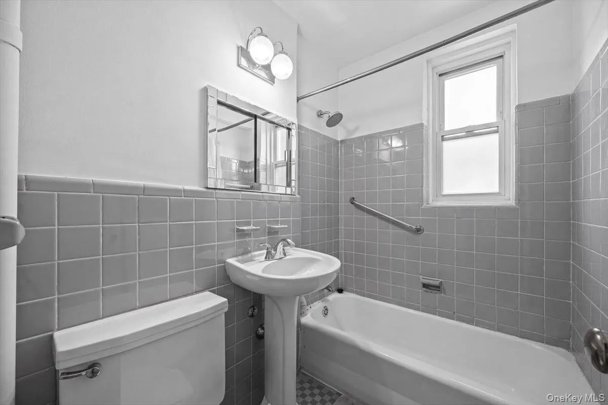 Bathroom featuring subway tile walls, a pedestal sink, and a combination shower/tub with a single-hung window Bathroom featuring subway tile walls, a pedestal sink, and a combination shower/tub with a single-hung window