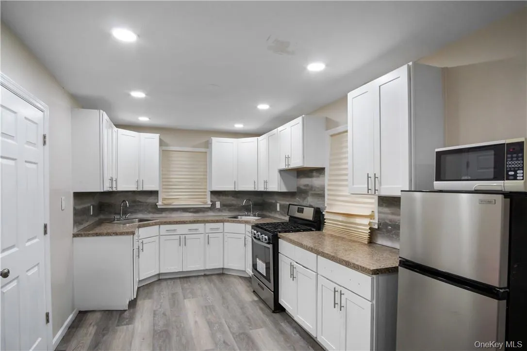 Kitchen featuring light hardwood / wood-style floors, appliances with stainless steel finishes, decorative backsplash, and sink Kitchen featuring light hardwood / wood-style floors, appliances with stainless steel finishes, decorative backsplash, and sink