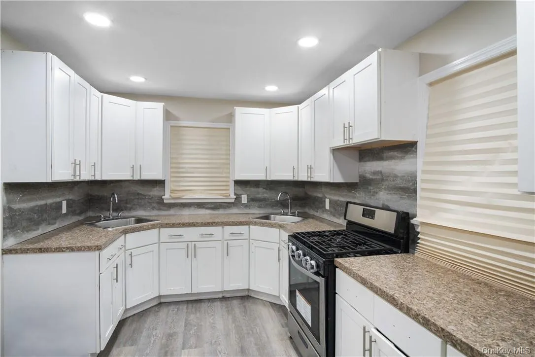 Kitchen with sink, stainless steel gas stove, decorative backsplash, light wood-type flooring, and white cabinetry Kitchen with sink, stainless steel gas stove, decorative backsplash, light wood-type flooring, and white cabinetry