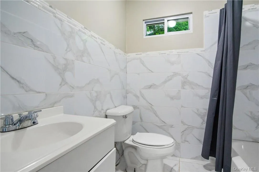 Full bathroom with shower / tub combo, tile walls, toilet, and vanity Full bathroom with shower / tub combo, tile walls, toilet, and vanity
