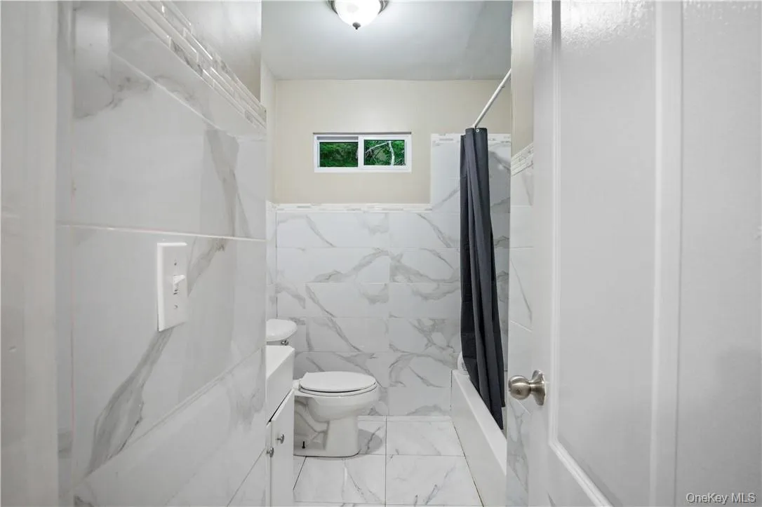Full bathroom featuring shower / bath combination with curtain, tile walls, tile patterned floors, toilet, and vanity Full bathroom featuring shower / bath combination with curtain, tile walls, tile patterned floors, toilet, and vanity