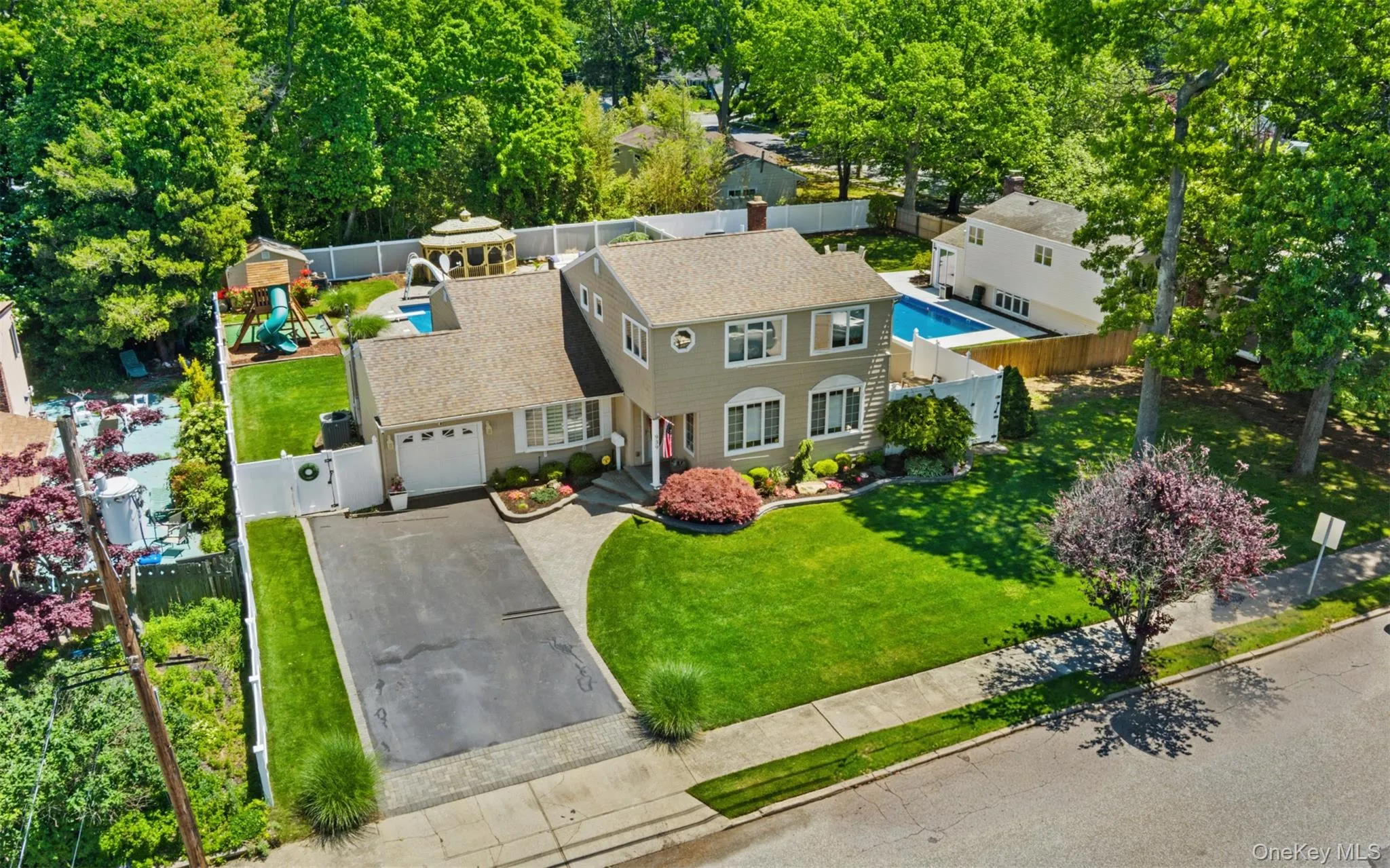 Two-story residence with a light gray facade and contrasting white trim, featuring a blacktop driveway and an attached garage Two-story residence with a light gray facade and contrasting white trim, featuring a blacktop driveway and an attached garage