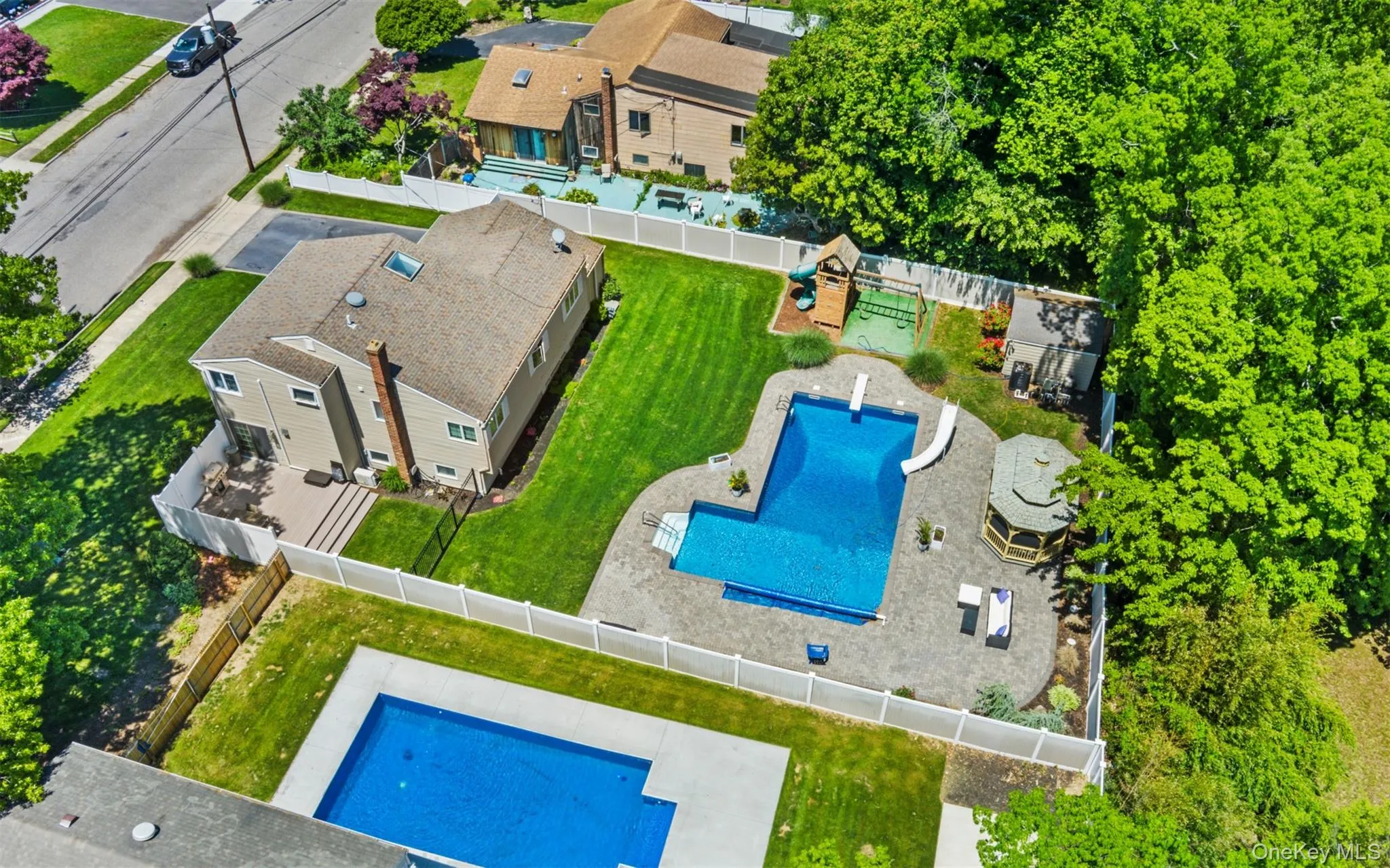Expansive backyard oasis featuring a custom-shaped swimming pool with a diving board, surrounding paver patio, and a dedicated shaded gazebo Expansive backyard oasis featuring a custom-shaped swimming pool with a diving board, surrounding paver patio, and a dedicated shaded gazebo