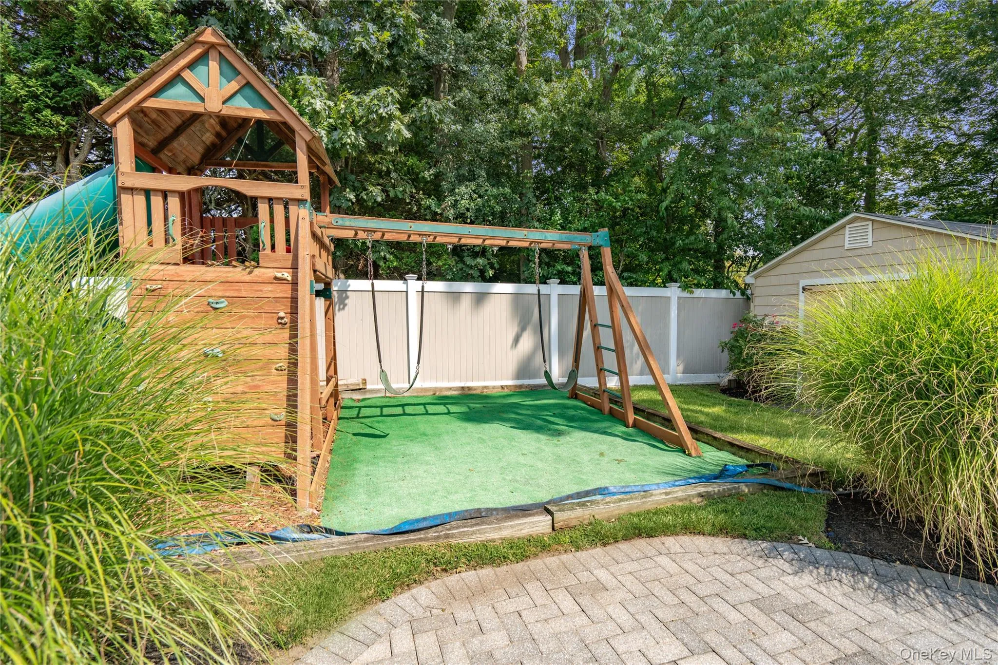 Backyard featuring a wooden playset with a climbing wall, swings, and an attached slide Backyard featuring a wooden playset with a climbing wall, swings, and an attached slide