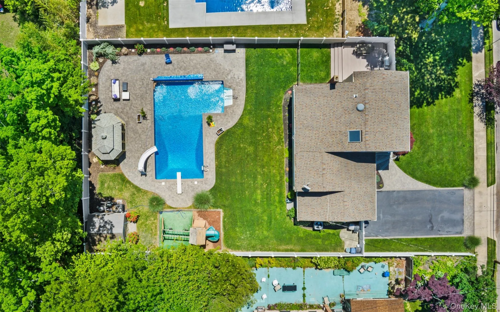 Expansive backyard featuring a large swimming pool with a diving board and curved slide, surrounded by a paver patio Expansive backyard featuring a large swimming pool with a diving board and curved slide, surrounded by a paver patio