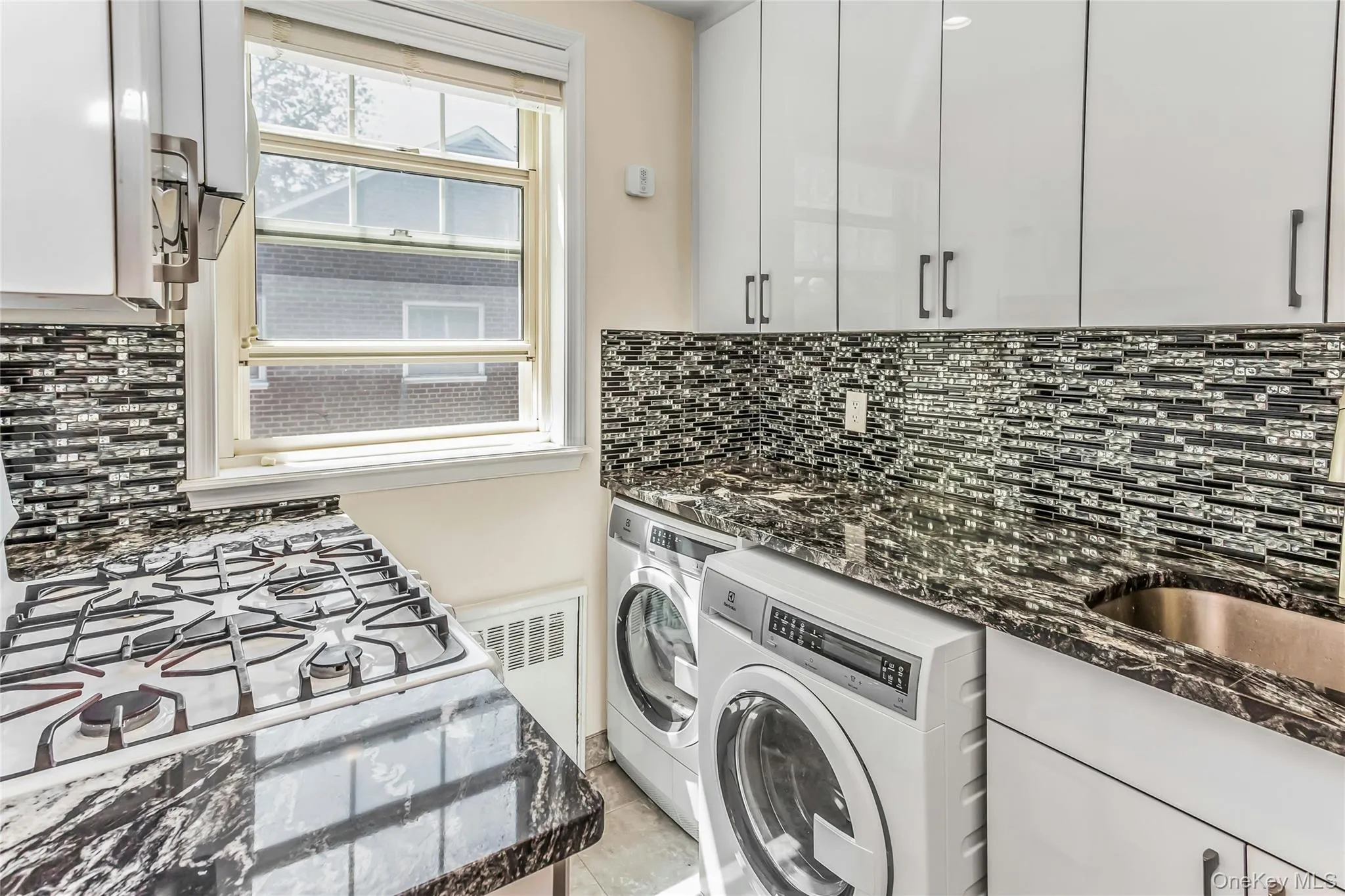 Kitchen area featuring high-gloss white cabinetry, dark stone countertops, and a patterned tile backsplash Kitchen area featuring high-gloss white cabinetry, dark stone countertops, and a patterned tile backsplash