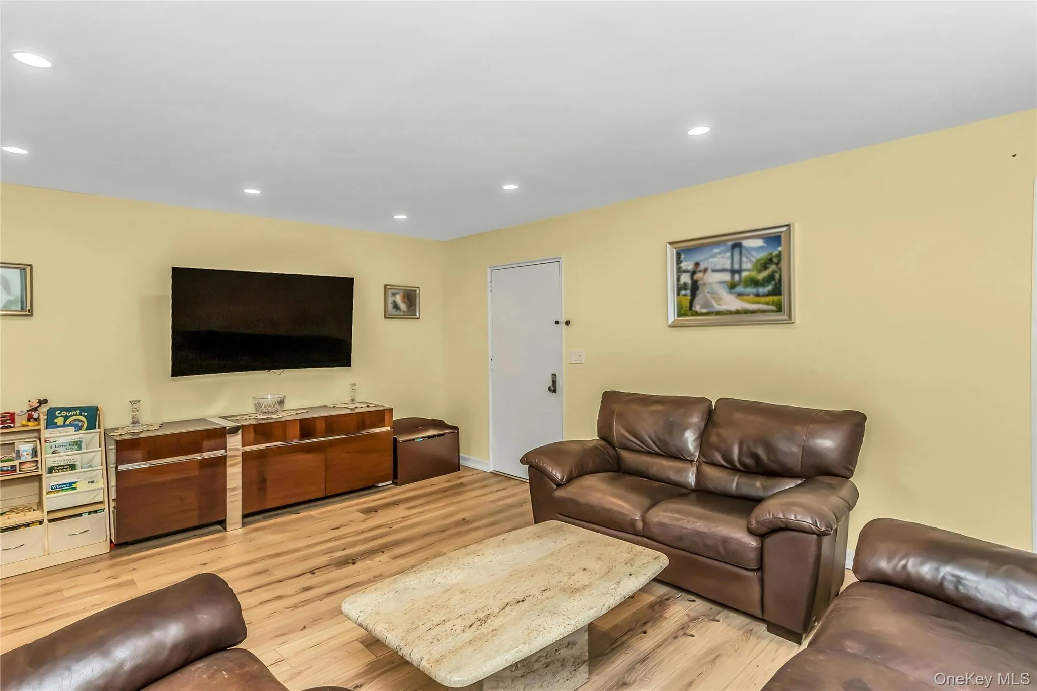 Spacious living area featuring wood-finish flooring, recessed lighting, a built-in wall-mounted television, and a built-in entertainment console with ample storage Spacious living area featuring wood-finish flooring, recessed lighting, a built-in wall-mounted television, and a built-in entertainment console with ample storage