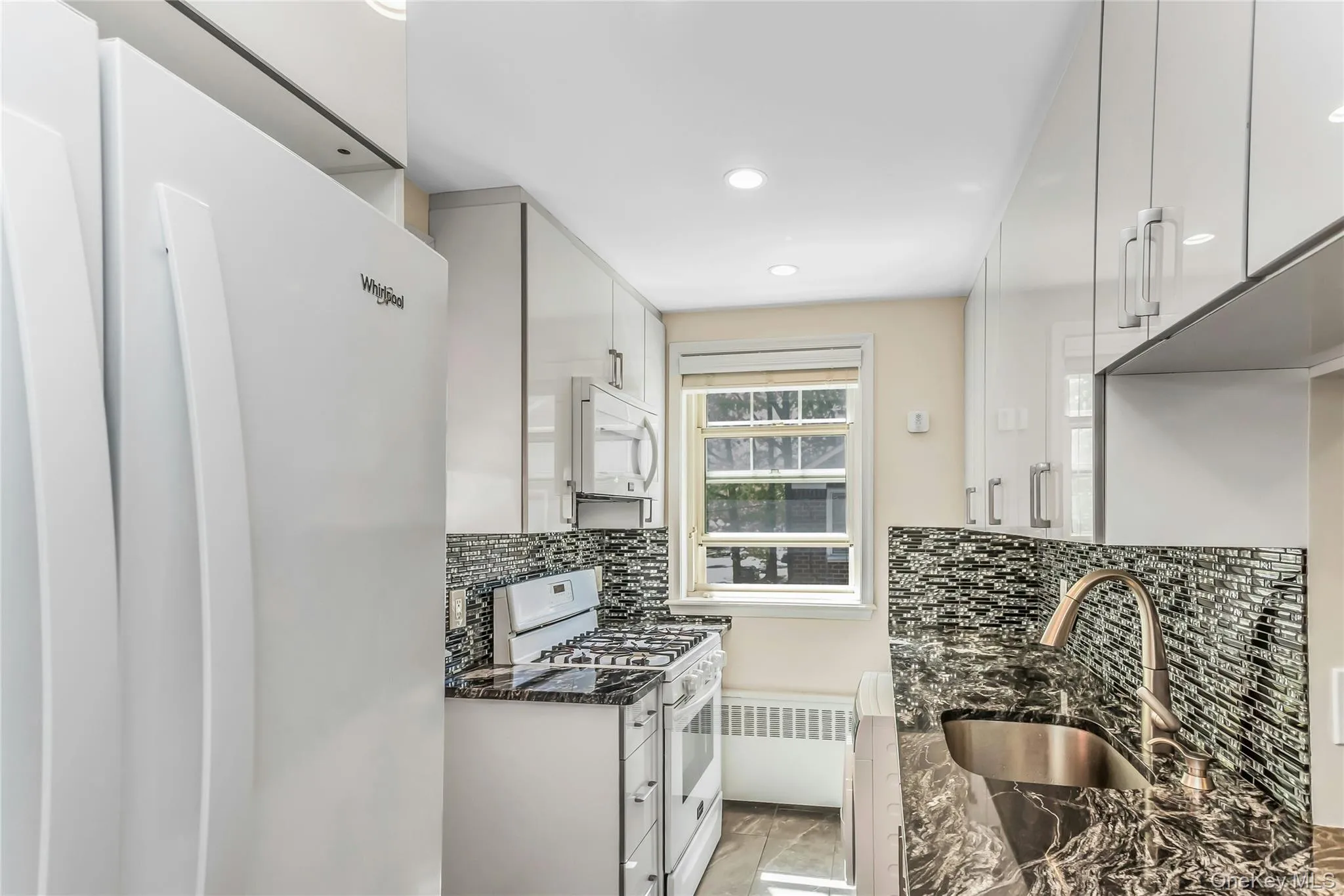 Galley kitchen featuring white appliances, glossy cabinetry, a tiled backsplash, and dark patterned countertops Galley kitchen featuring white appliances, glossy cabinetry, a tiled backsplash, and dark patterned countertops