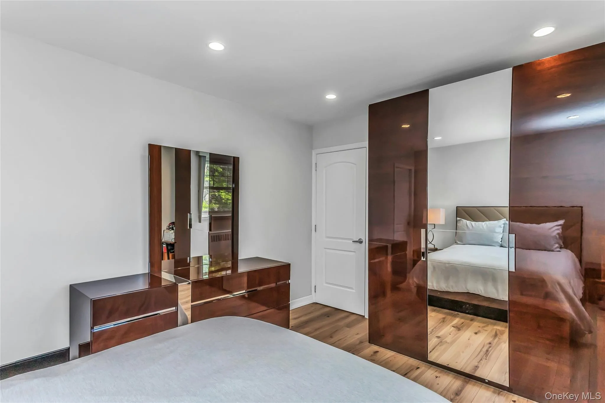 Recessed lighting illuminates a space featuring wood-finish flooring and a white paneled door with contemporary hardware Recessed lighting illuminates a space featuring wood-finish flooring and a white paneled door with contemporary hardware