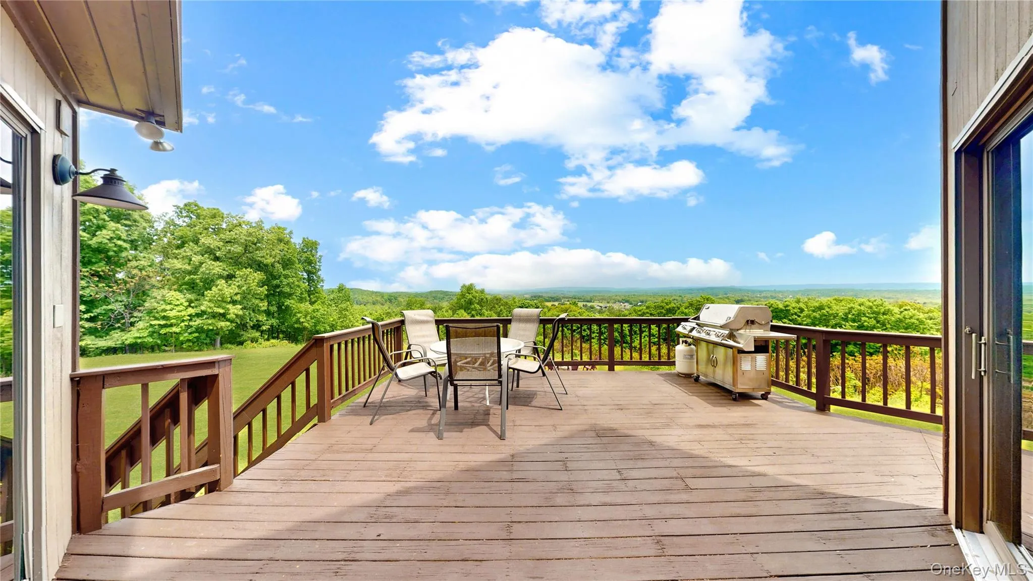 Expansive wood-finish deck with perimeter railing and outdoor wall-mounted lighting Expansive wood-finish deck with perimeter railing and outdoor wall-mounted lighting