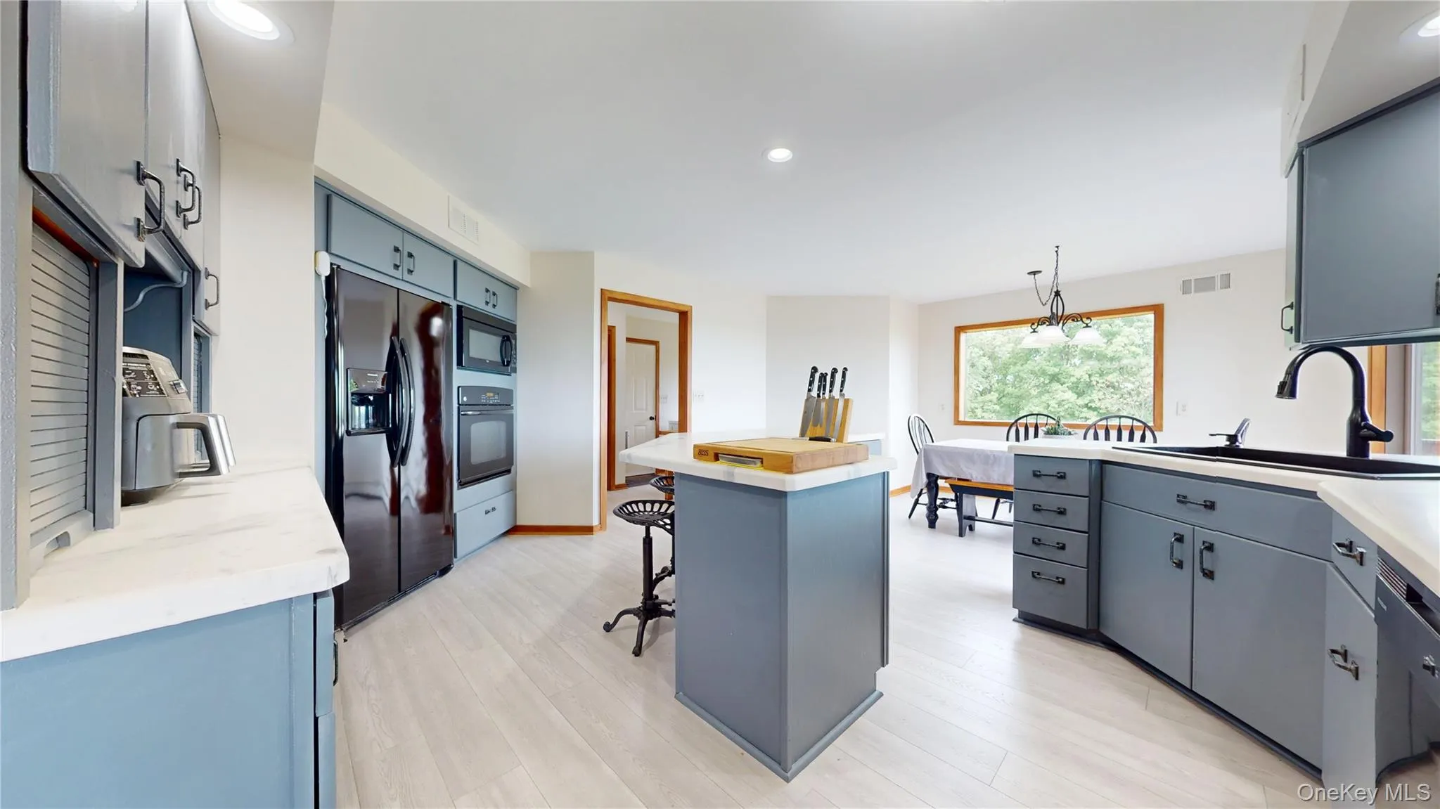 Open-concept kitchen featuring light-toned wood-finish flooring, custom blue cabinetry with dark hardware, recessed lighting, and a kitchen island with a light-toned countertop Open-concept kitchen featuring light-toned wood-finish flooring, custom blue cabinetry with dark hardware, recessed lighting, and a kitchen island with a light-toned countertop