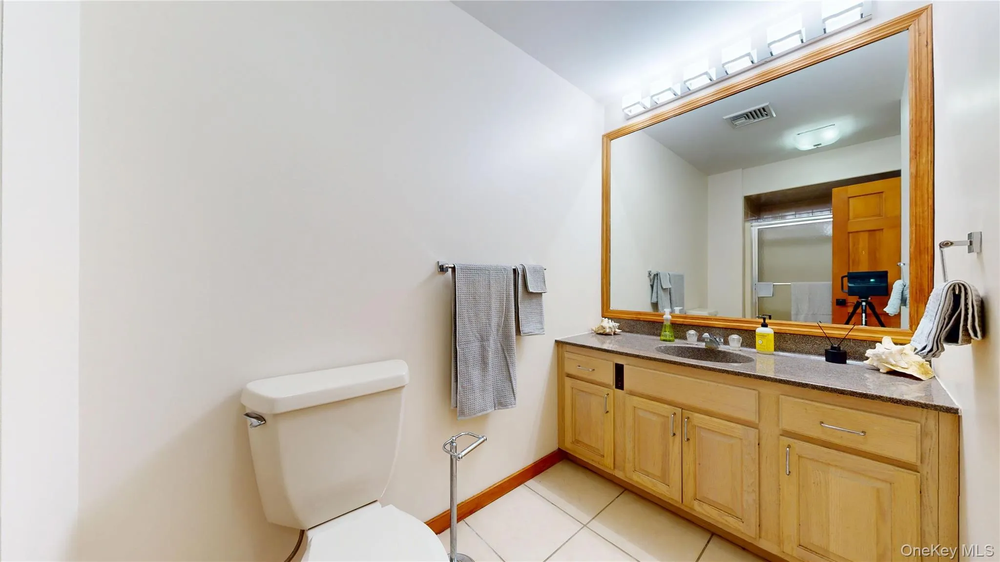 Bathroom featuring a wood-framed mirror, a light wood vanity with an integrated sink, a dark countertop, and tiled flooring Bathroom featuring a wood-framed mirror, a light wood vanity with an integrated sink, a dark countertop, and tiled flooring