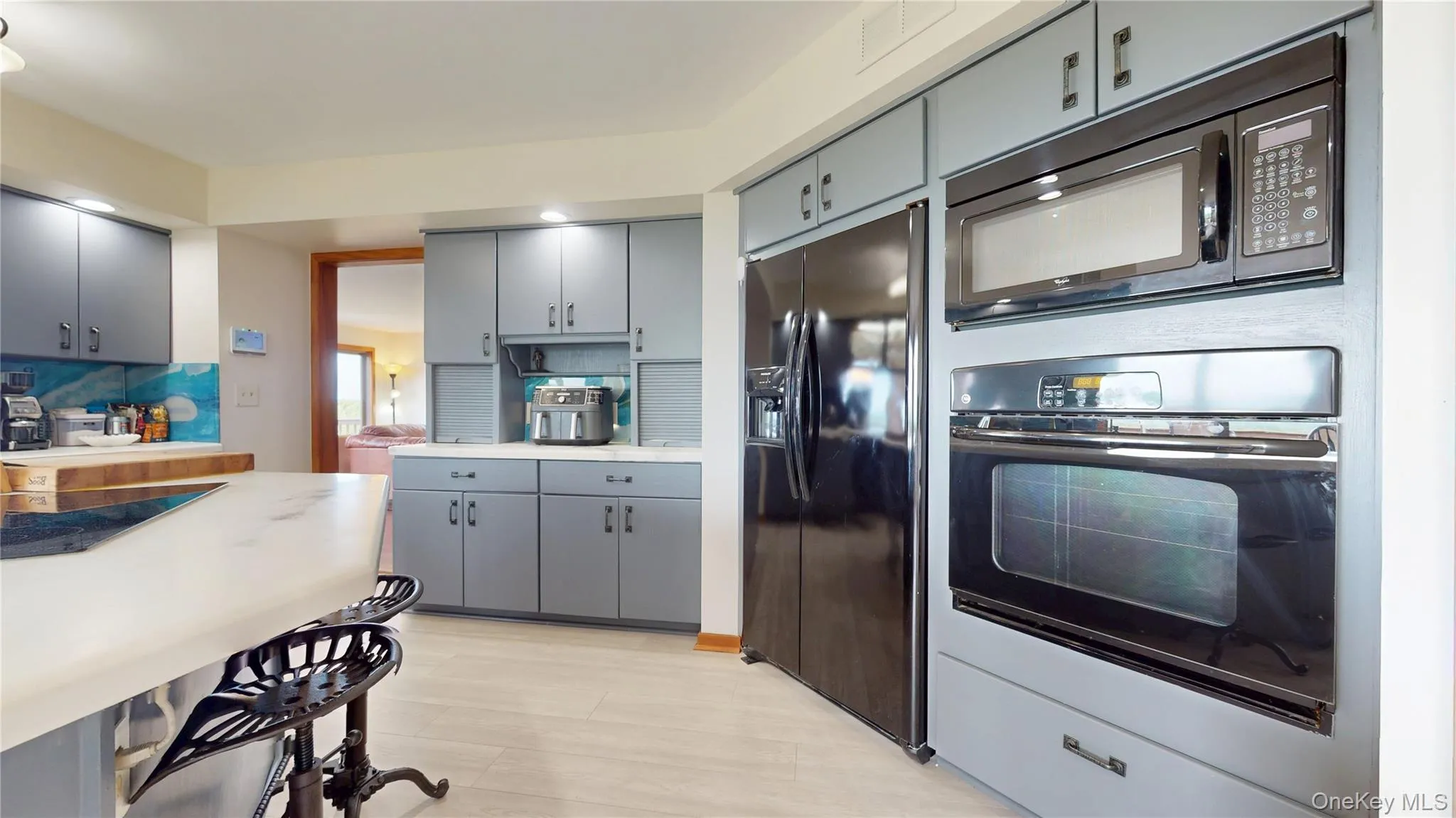 Kitchen featuring light gray cabinetry, built-in microwave, wall oven, black side-by-side refrigerator, and light wood-finish flooring Kitchen featuring light gray cabinetry, built-in microwave, wall oven, black side-by-side refrigerator, and light wood-finish flooring