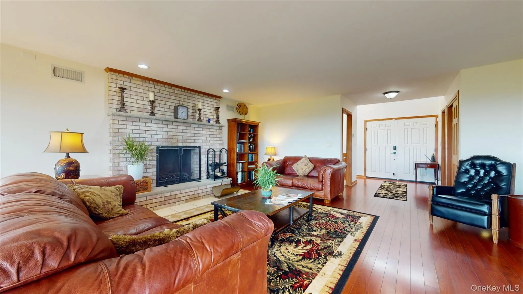 Spacious living area featuring a brick fireplace with a raised hearth, recessed lighting, and wood-finish flooring Spacious living area featuring a brick fireplace with a raised hearth, recessed lighting, and wood-finish flooring