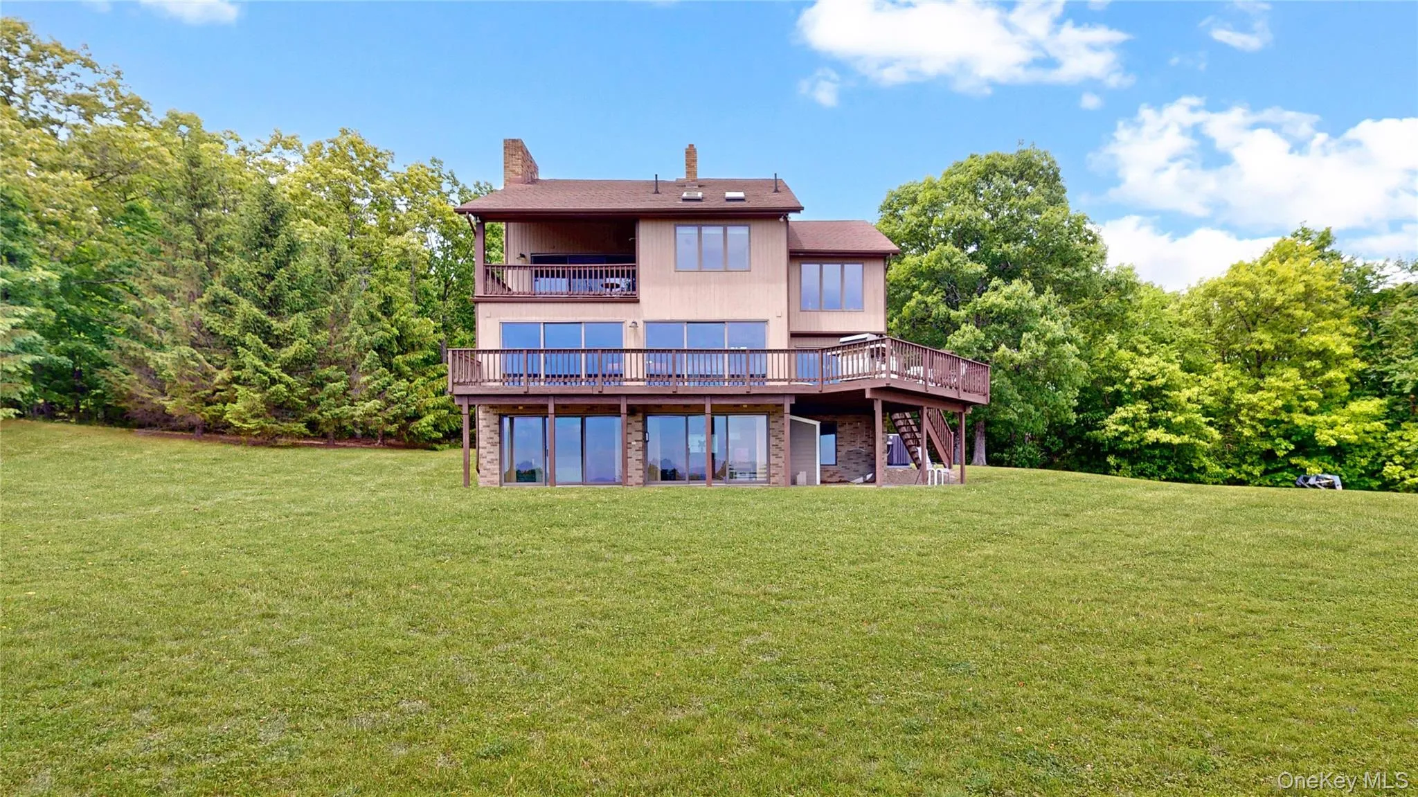 Multi-level home featuring extensive decking, a lower-level patio, and a prominent brick chimney Multi-level home featuring extensive decking, a lower-level patio, and a prominent brick chimney