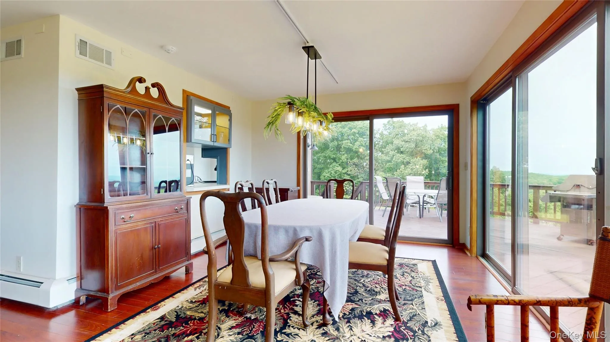 Dining area featuring wood-finish flooring, two sets of sliding glass doors opening to a large exterior deck, and a built-in illuminated hutch Dining area featuring wood-finish flooring, two sets of sliding glass doors opening to a large exterior deck, and a built-in illuminated hutch
