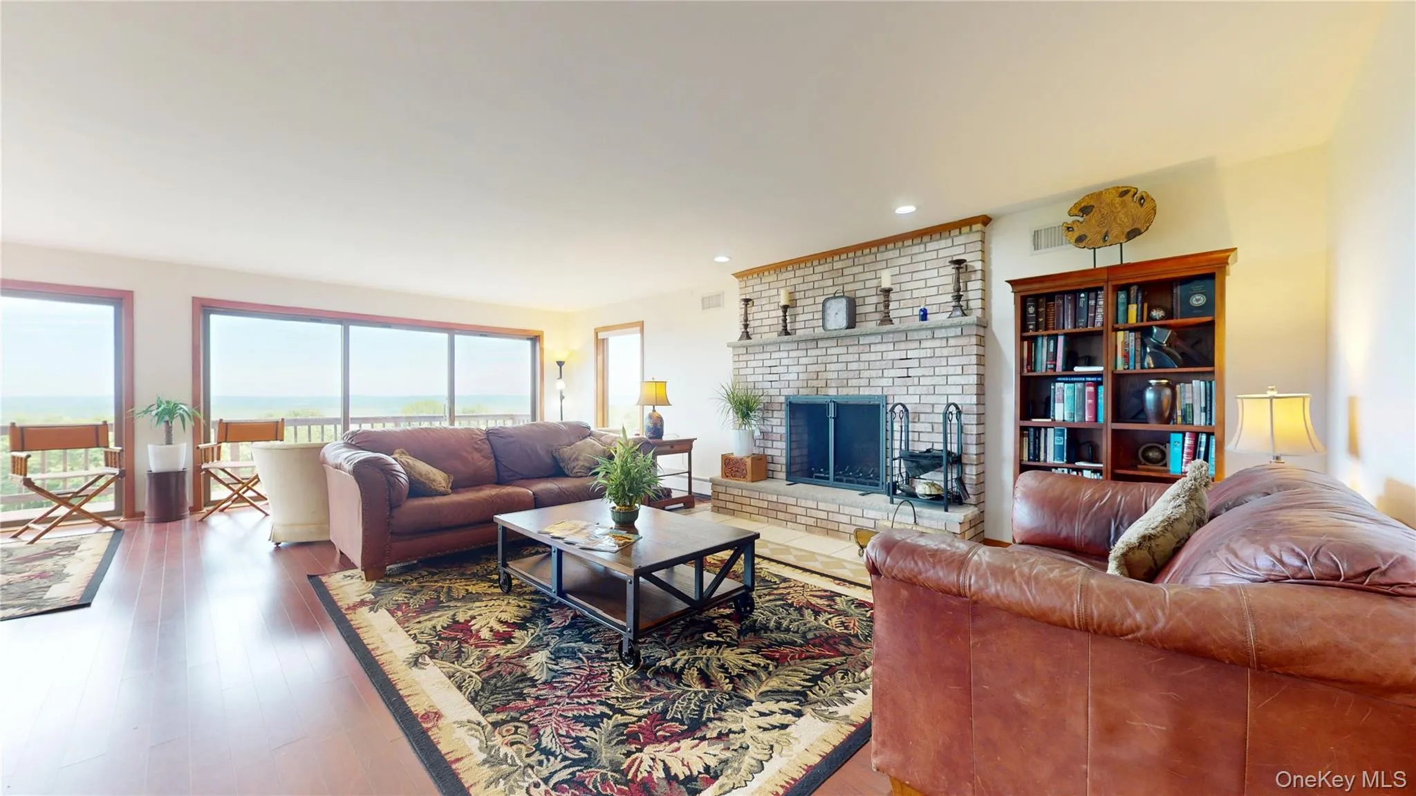 Living area featuring expansive windows, wood-finish flooring, a brick fireplace with a hearth, and built-in shelving Living area featuring expansive windows, wood-finish flooring, a brick fireplace with a hearth, and built-in shelving