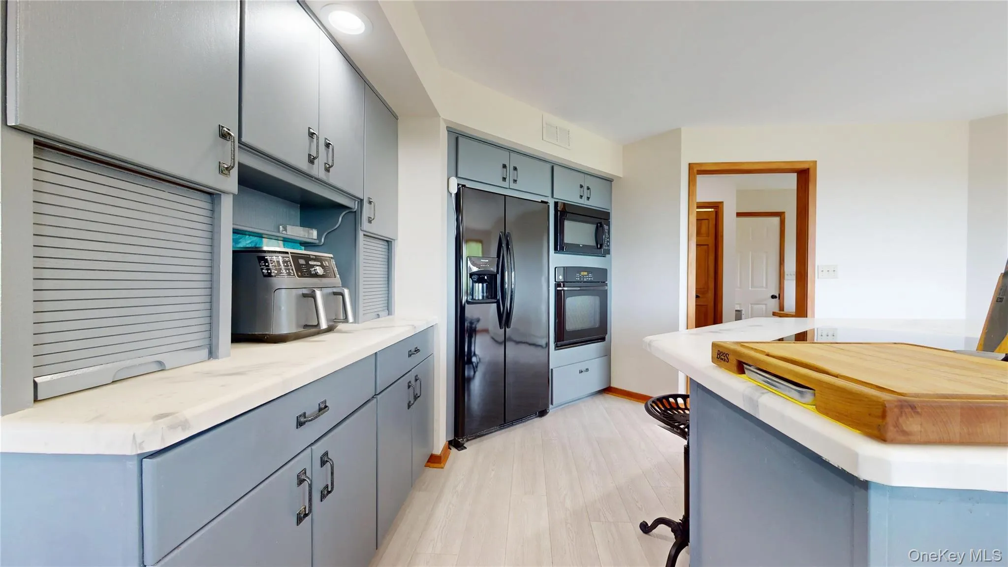 Kitchen featuring light blue cabinetry, white countertops, wood-finish flooring, and black appliances including a refrigerator, microwave, and built-in oven Kitchen featuring light blue cabinetry, white countertops, wood-finish flooring, and black appliances including a refrigerator, microwave, and built-in oven