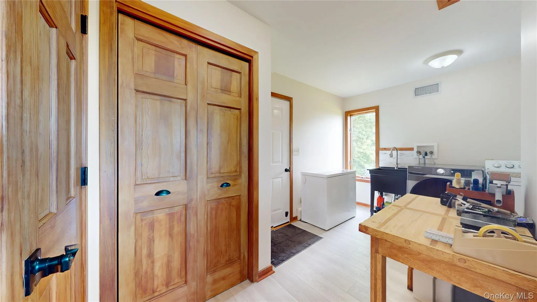 Laundry area featuring wood-finish flooring, a utility sink, and a window providing natural light Laundry area featuring wood-finish flooring, a utility sink, and a window providing natural light