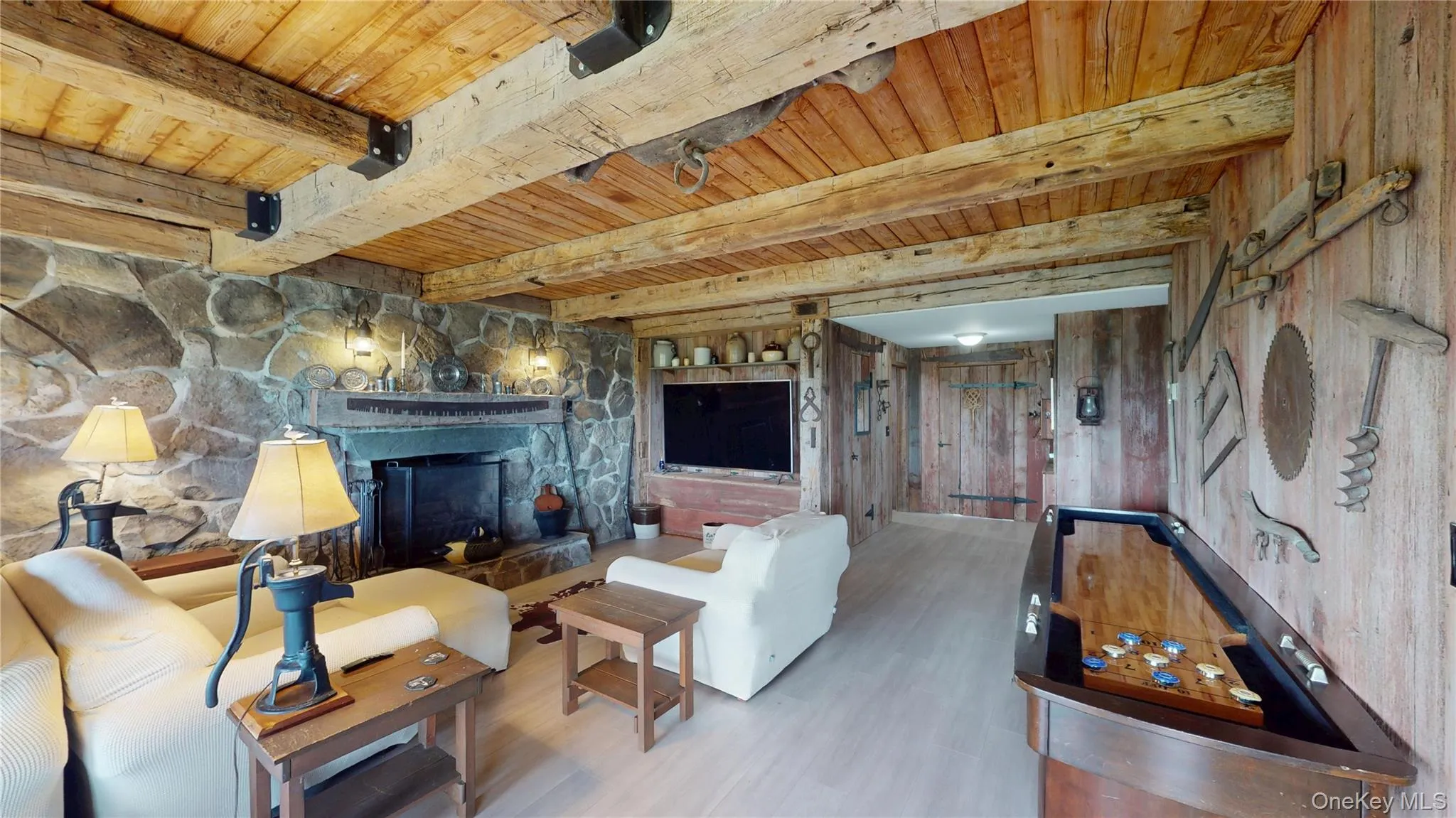 Exposed wood beam ceiling with recessed panels, stone fireplace with hearth, built-in media center, wood-finish flooring, and natural wood plank wall finishes Exposed wood beam ceiling with recessed panels, stone fireplace with hearth, built-in media center, wood-finish flooring, and natural wood plank wall finishes