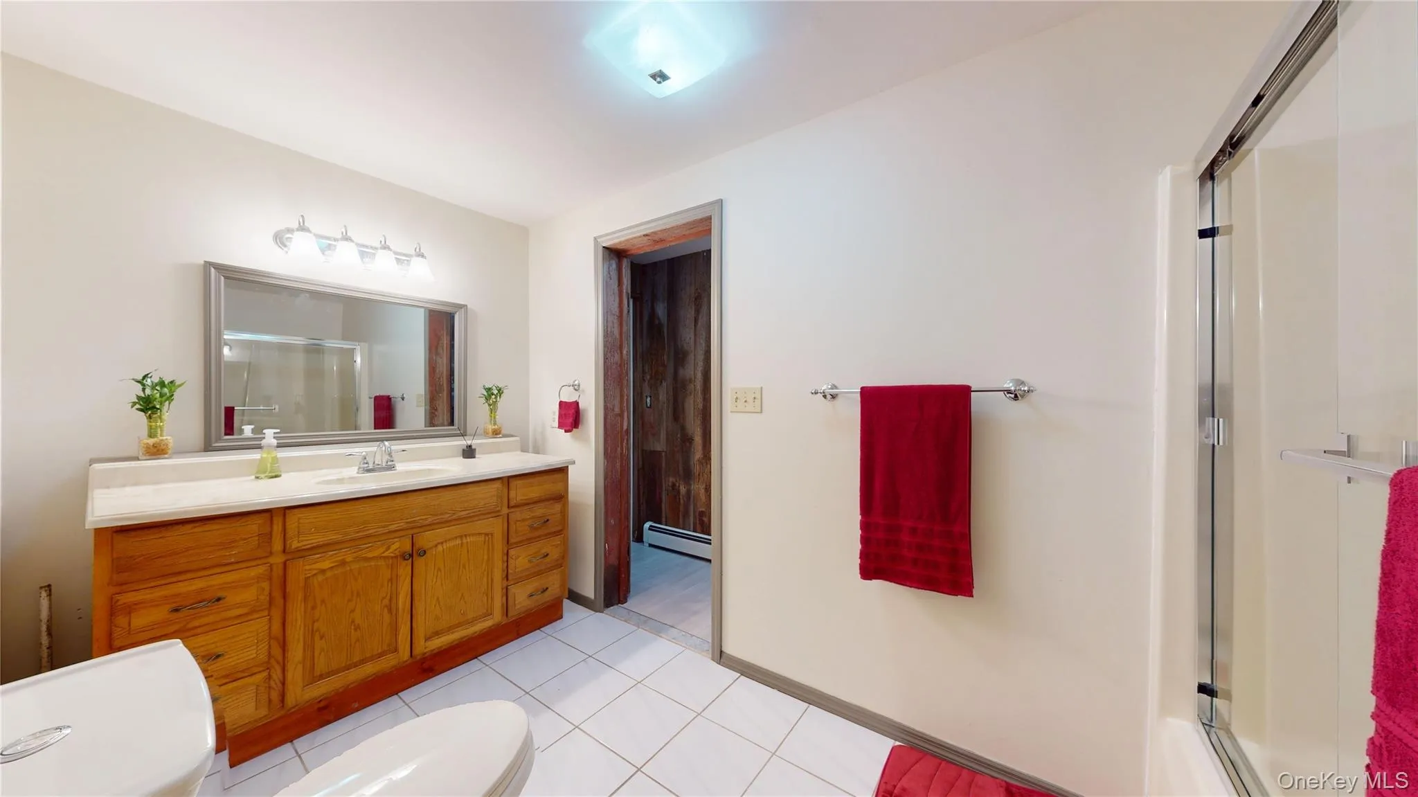 Bathroom featuring a wood vanity with a light-toned countertop, a framed mirror, and a five-light fixture Bathroom featuring a wood vanity with a light-toned countertop, a framed mirror, and a five-light fixture