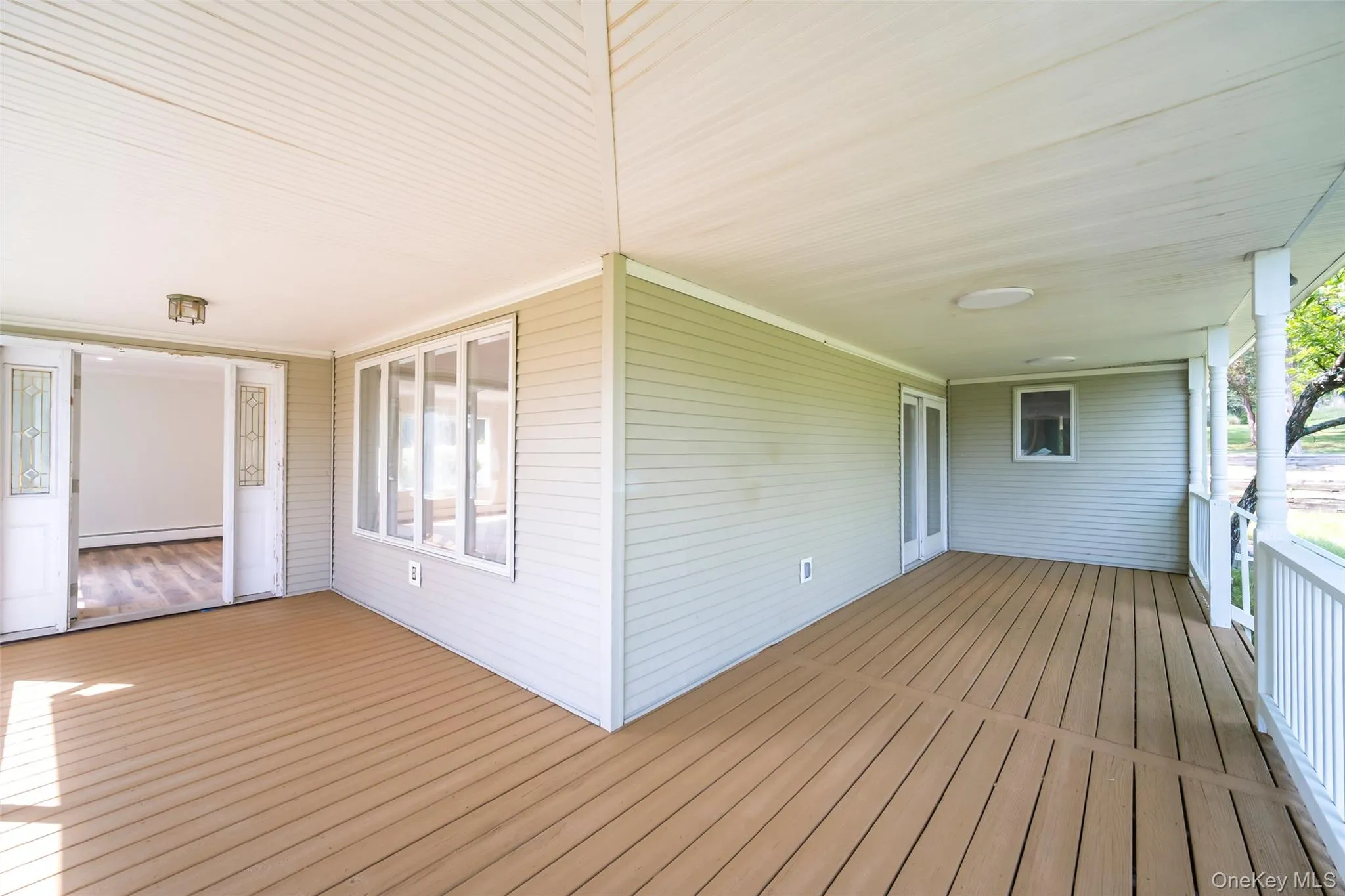 Expansive covered porch featuring wood-finish decking, white railings, and a beadboard ceiling Expansive covered porch featuring wood-finish decking, white railings, and a beadboard ceiling