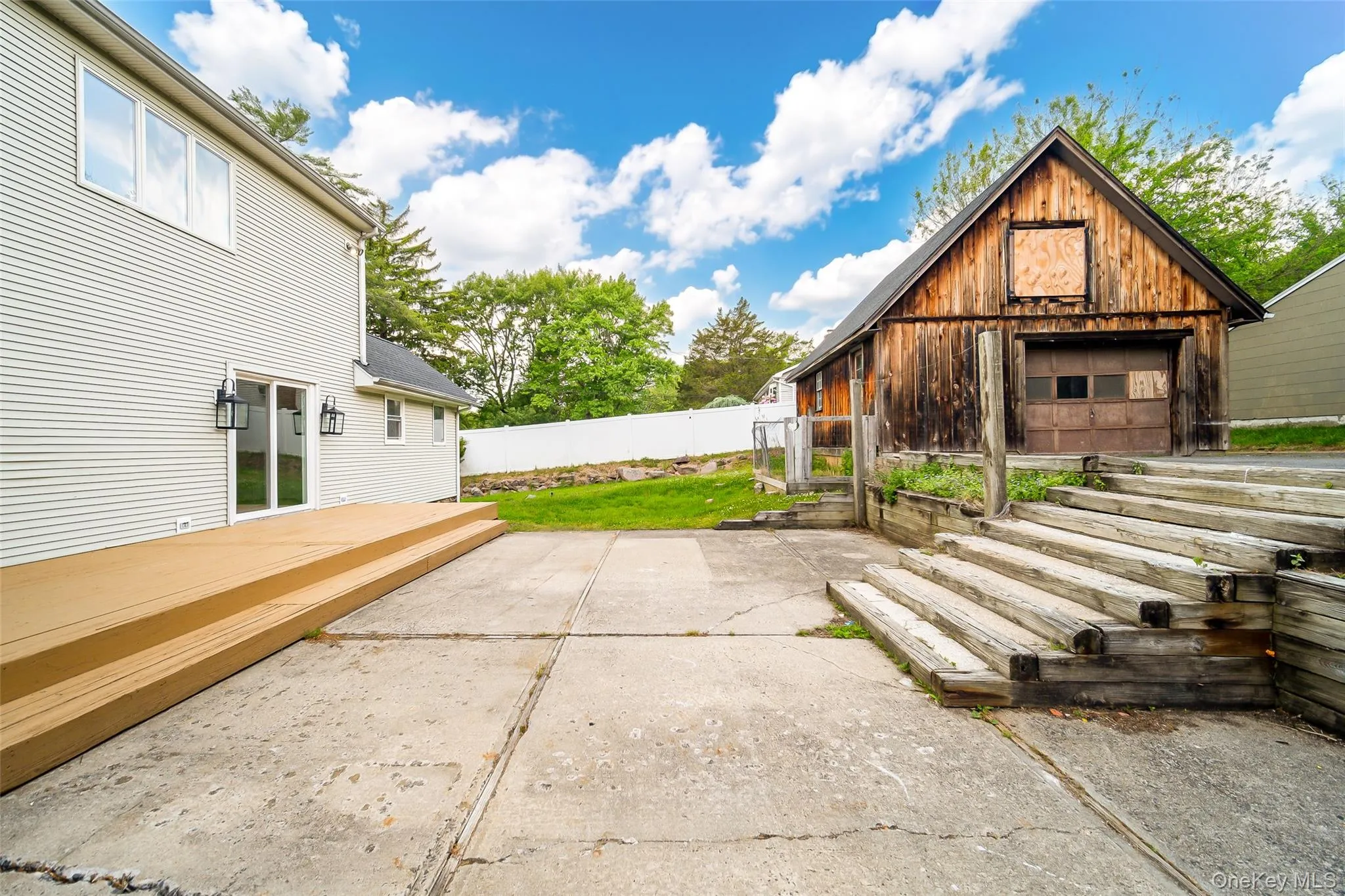 Rear exterior featuring a large ground-level deck, concrete patio, and a rustic detached barn structure Rear exterior featuring a large ground-level deck, concrete patio, and a rustic detached barn structure