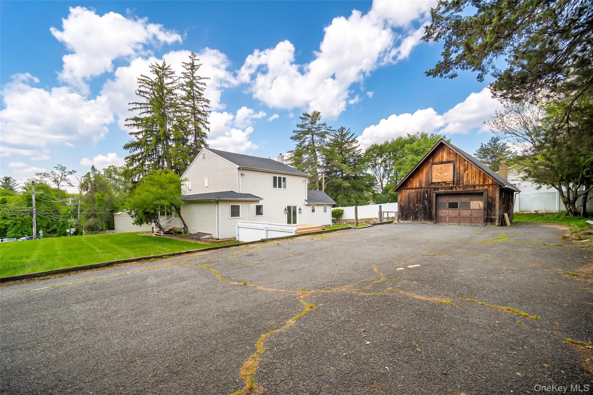 Property exterior featuring a two-story residence with light-colored siding and a dark roof, accompanied by a detached wooden barn with a single garage door Property exterior featuring a two-story residence with light-colored siding and a dark roof, accompanied by a detached wooden barn with a single garage door