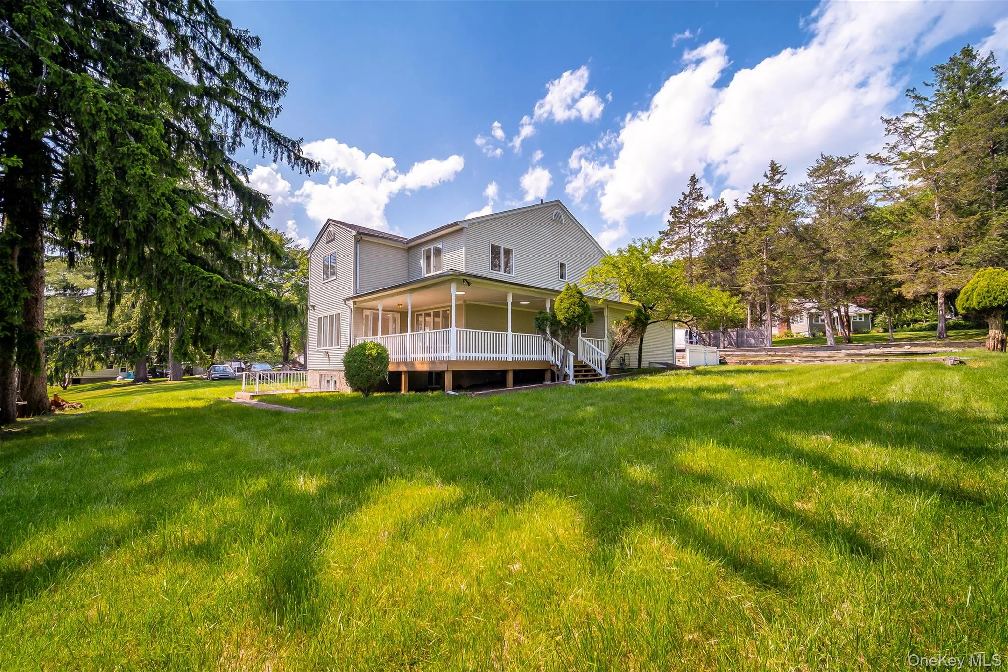 Expansive backyard with a manicured lawn, mature trees, and a spacious covered porch featuring white railings Expansive backyard with a manicured lawn, mature trees, and a spacious covered porch featuring white railings