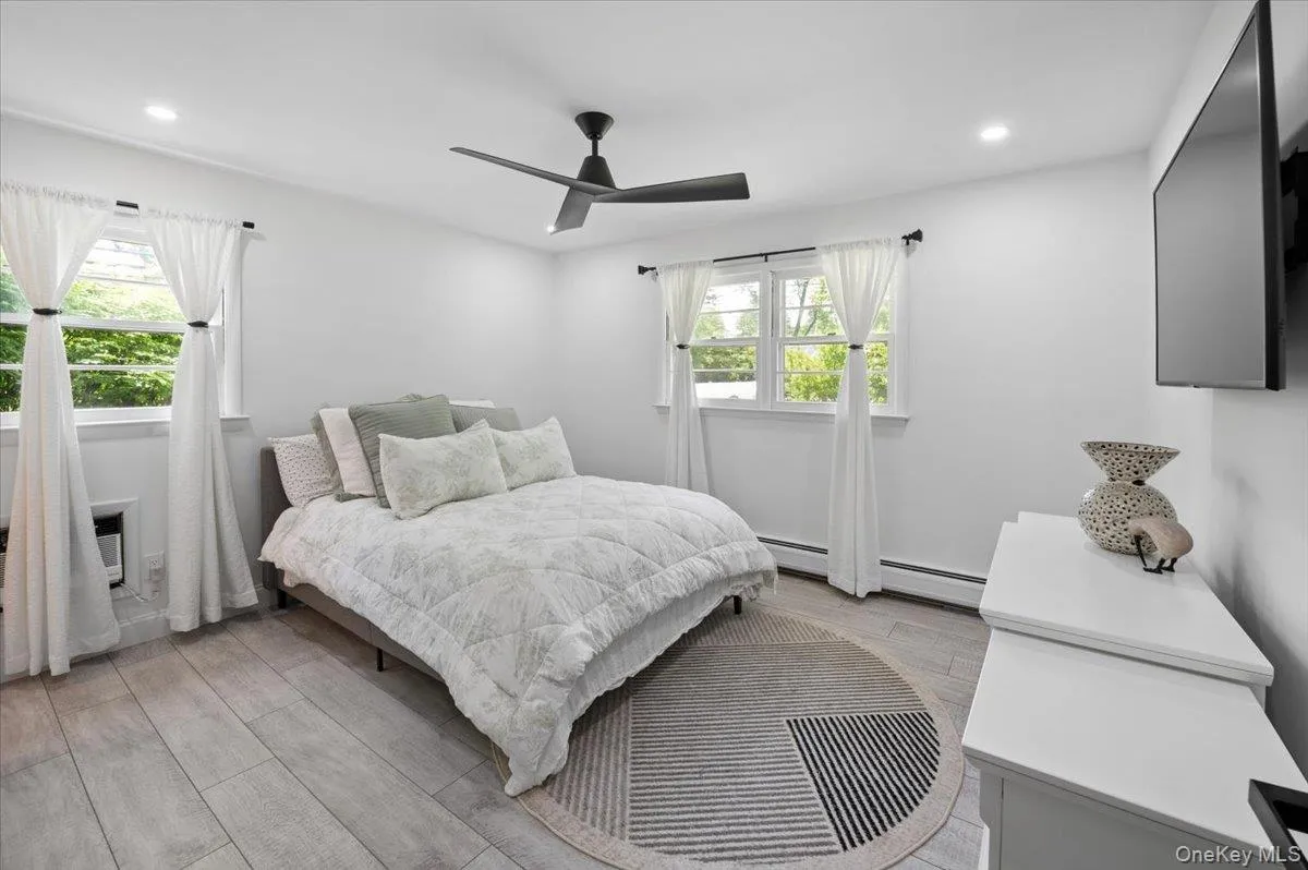 Light wood-finish flooring complements the crisp white walls in this bedroom, featuring two windows with white trim and a ceiling fan with integrated lighting. Light wood-finish flooring complements the crisp white walls in this bedroom, featuring two windows with white trim and a ceiling fan with integrated lighting.