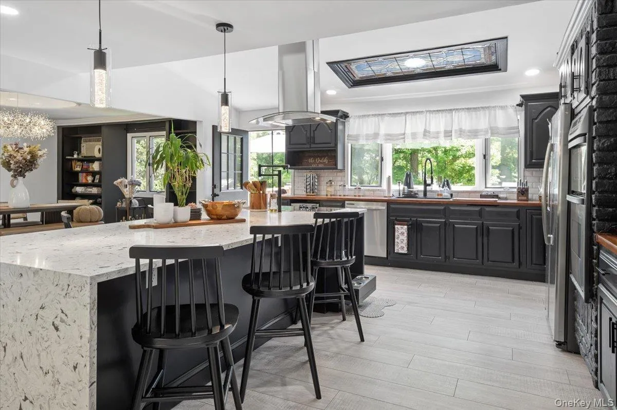 Spacious kitchen featuring a large waterfall-edge island with seating, a built-in oven, black cabinetry, and wood-finish countertops. Spacious kitchen featuring a large waterfall-edge island with seating, a built-in oven, black cabinetry, and wood-finish countertops.