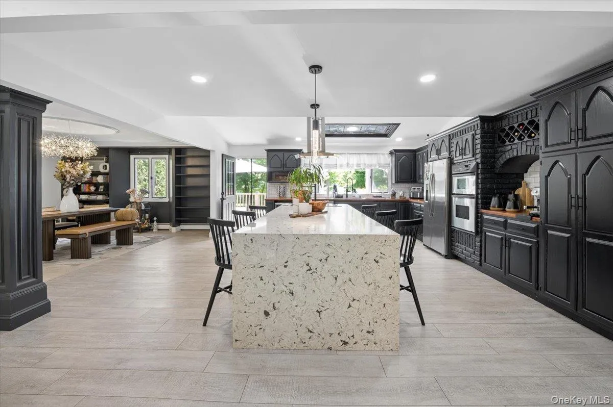 Expansive kitchen featuring a large waterfall-edge island, black cabinetry, integrated wine storage, and a built-in oven. Expansive kitchen featuring a large waterfall-edge island, black cabinetry, integrated wine storage, and a built-in oven.