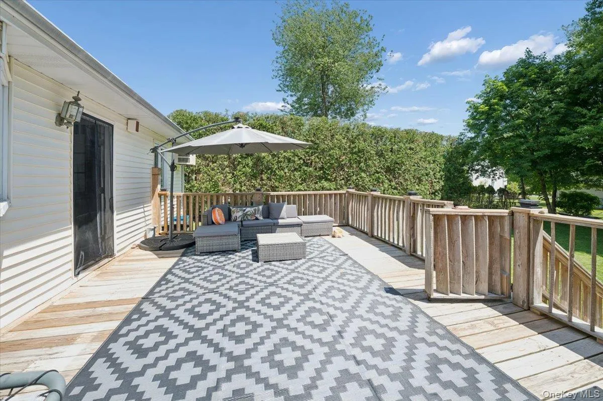 Expansive wood deck with natural wood railings, featuring a privacy hedge, and white siding exterior. Expansive wood deck with natural wood railings, featuring a privacy hedge, and white siding exterior.