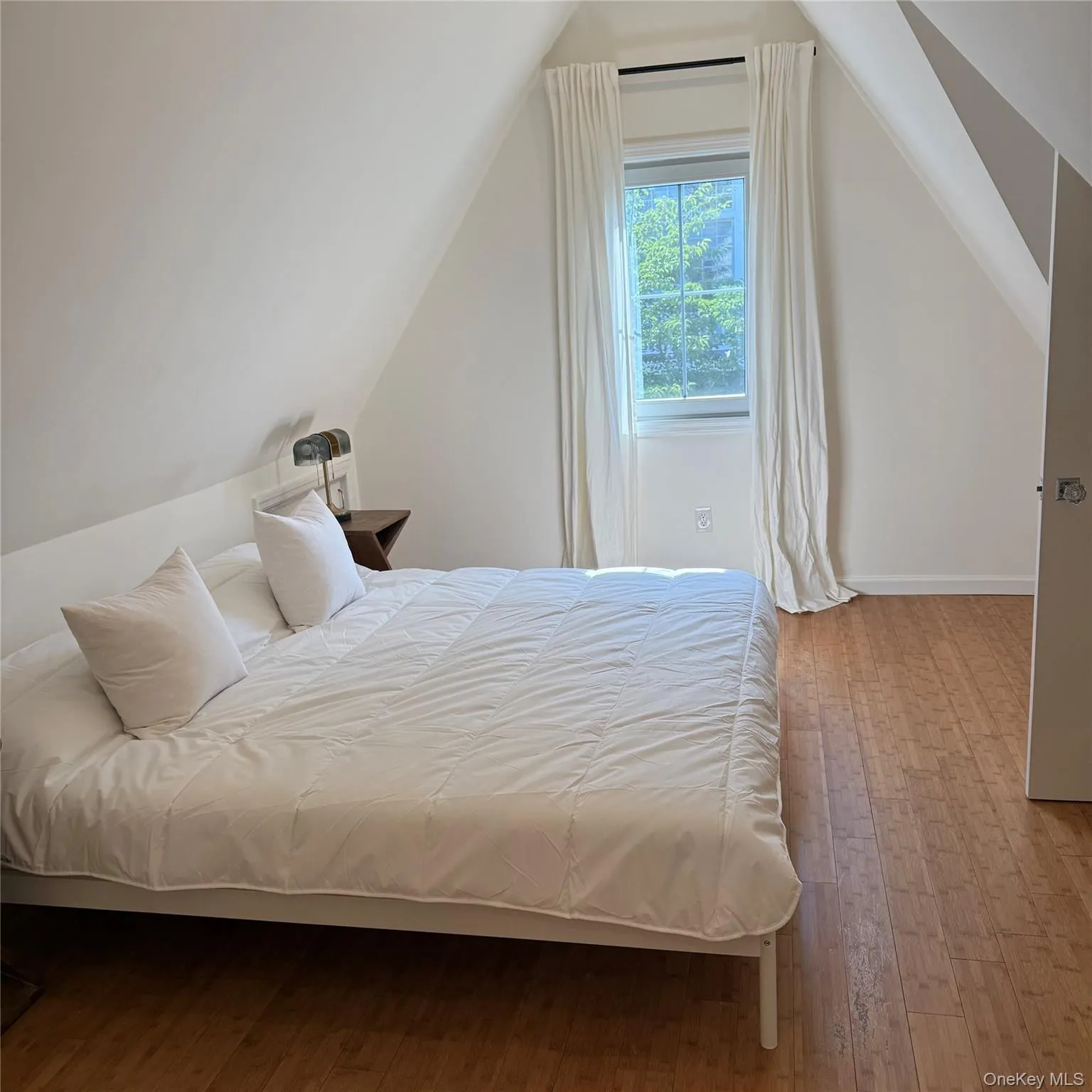Angled ceiling lines with a window, wood-finish flooring, and a white interior door Angled ceiling lines with a window, wood-finish flooring, and a white interior door