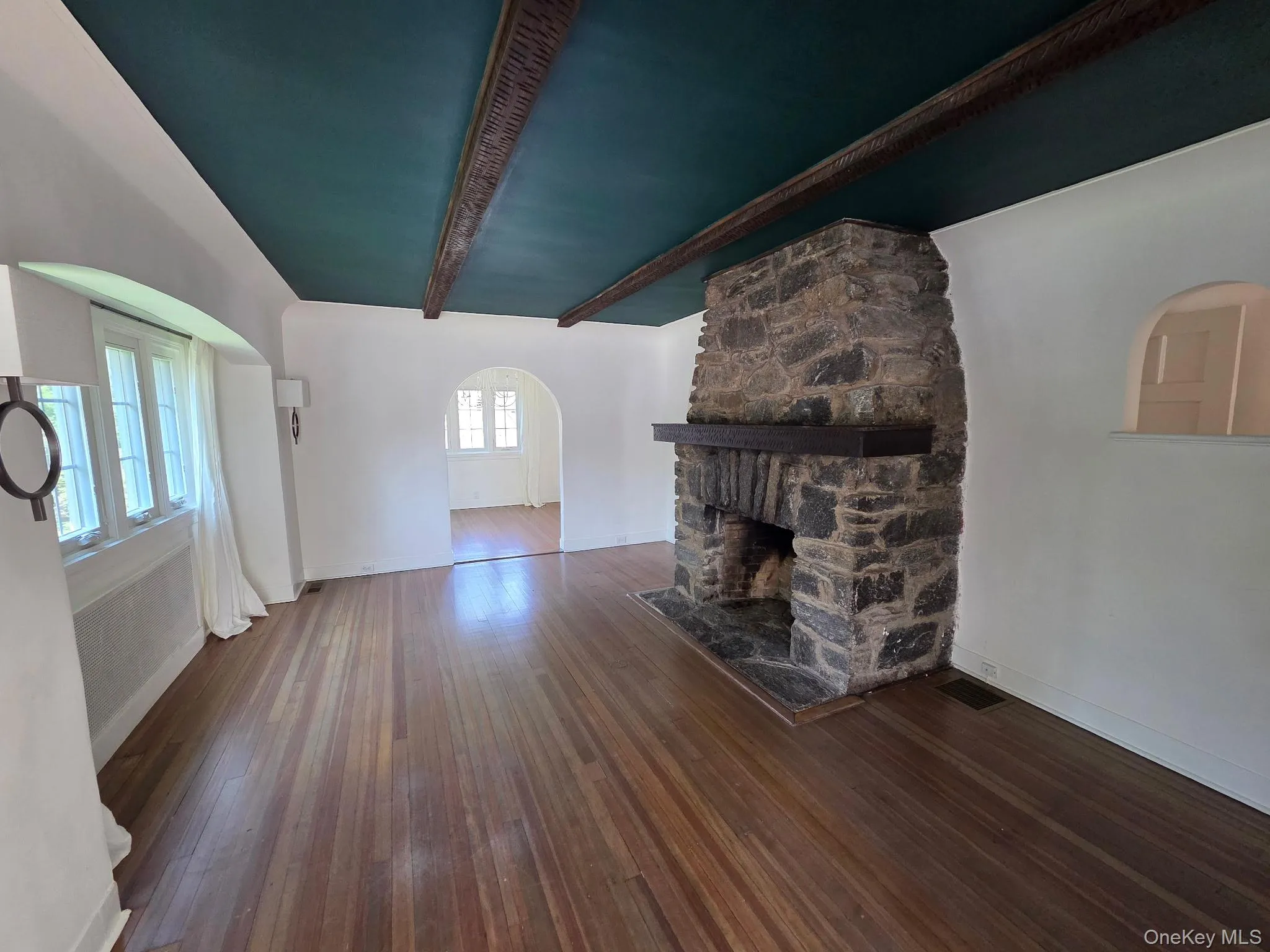Stone fireplace with dark wood mantel, wide plank wood-finish flooring, and arched doorways Stone fireplace with dark wood mantel, wide plank wood-finish flooring, and arched doorways
