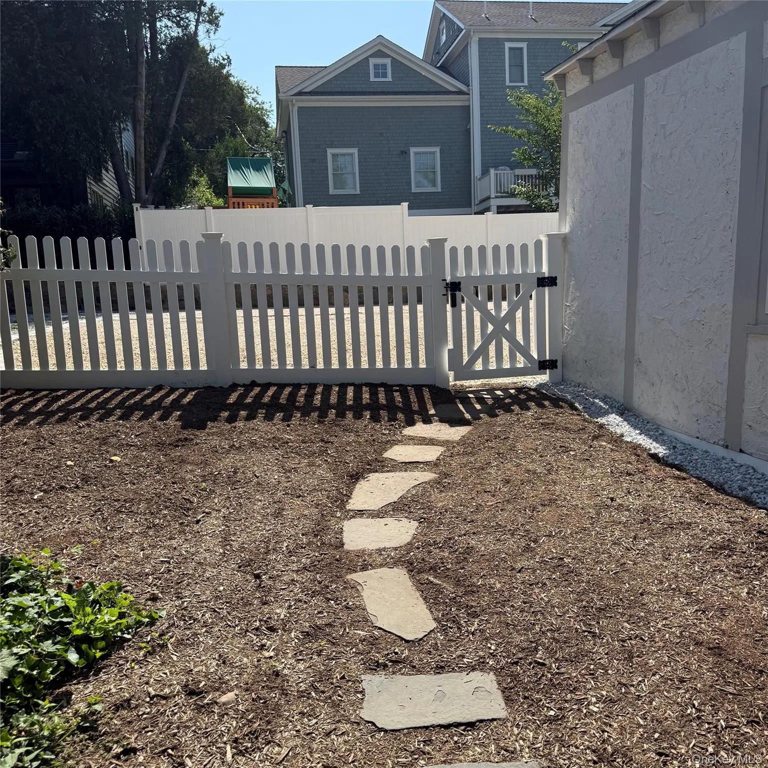 White picket fence with gate, stepping stone pathway, and mulched ground cover White picket fence with gate, stepping stone pathway, and mulched ground cover