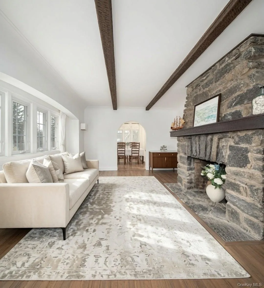 Exposed ceiling beams, expansive window bank, stone-clad fireplace, wood-finish flooring, and an arched doorway Exposed ceiling beams, expansive window bank, stone-clad fireplace, wood-finish flooring, and an arched doorway