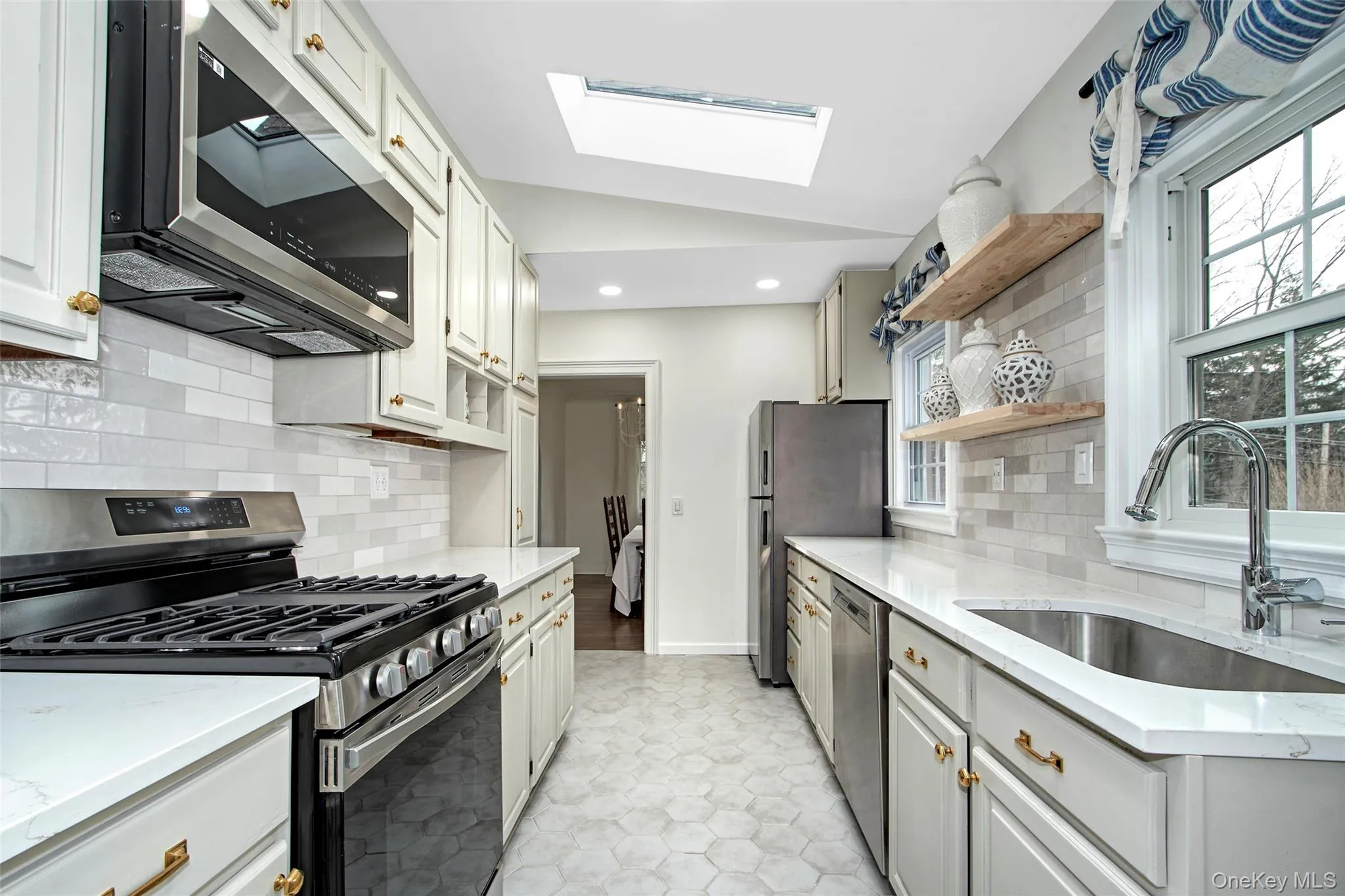 Kitchen featuring sink, lofted ceiling with skylight, stainless steel appliances, white cabinets, and decorative backsplash Kitchen featuring sink, lofted ceiling with skylight, stainless steel appliances, white cabinets, and decorative backsplash