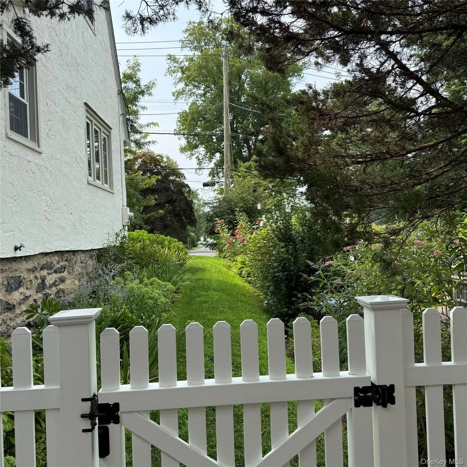 White picket fence with black hardware, leading to a grassy area for pets and family White picket fence with black hardware, leading to a grassy area for pets and family